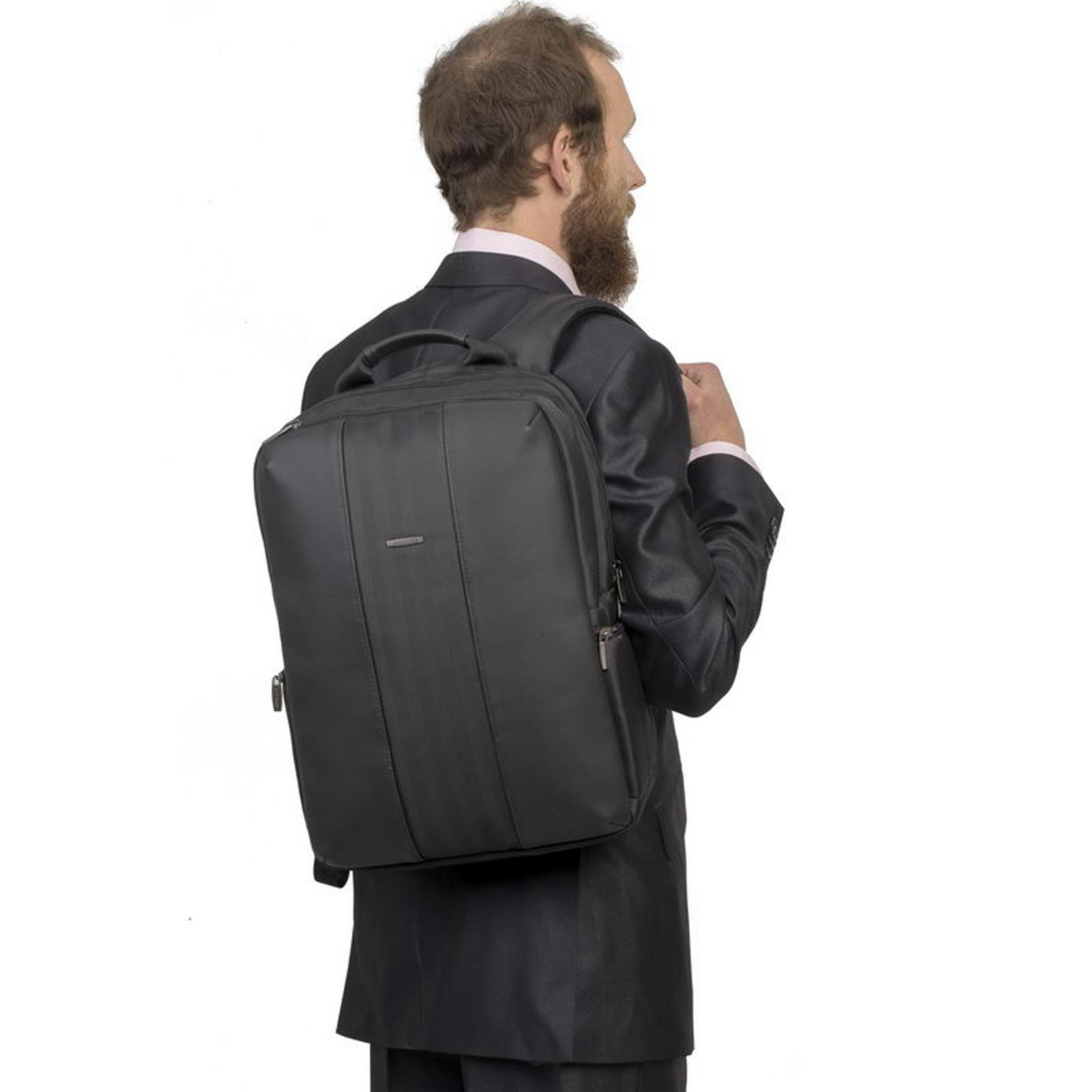 Un uomo con la barba in abito nero porta uno zaino nero.