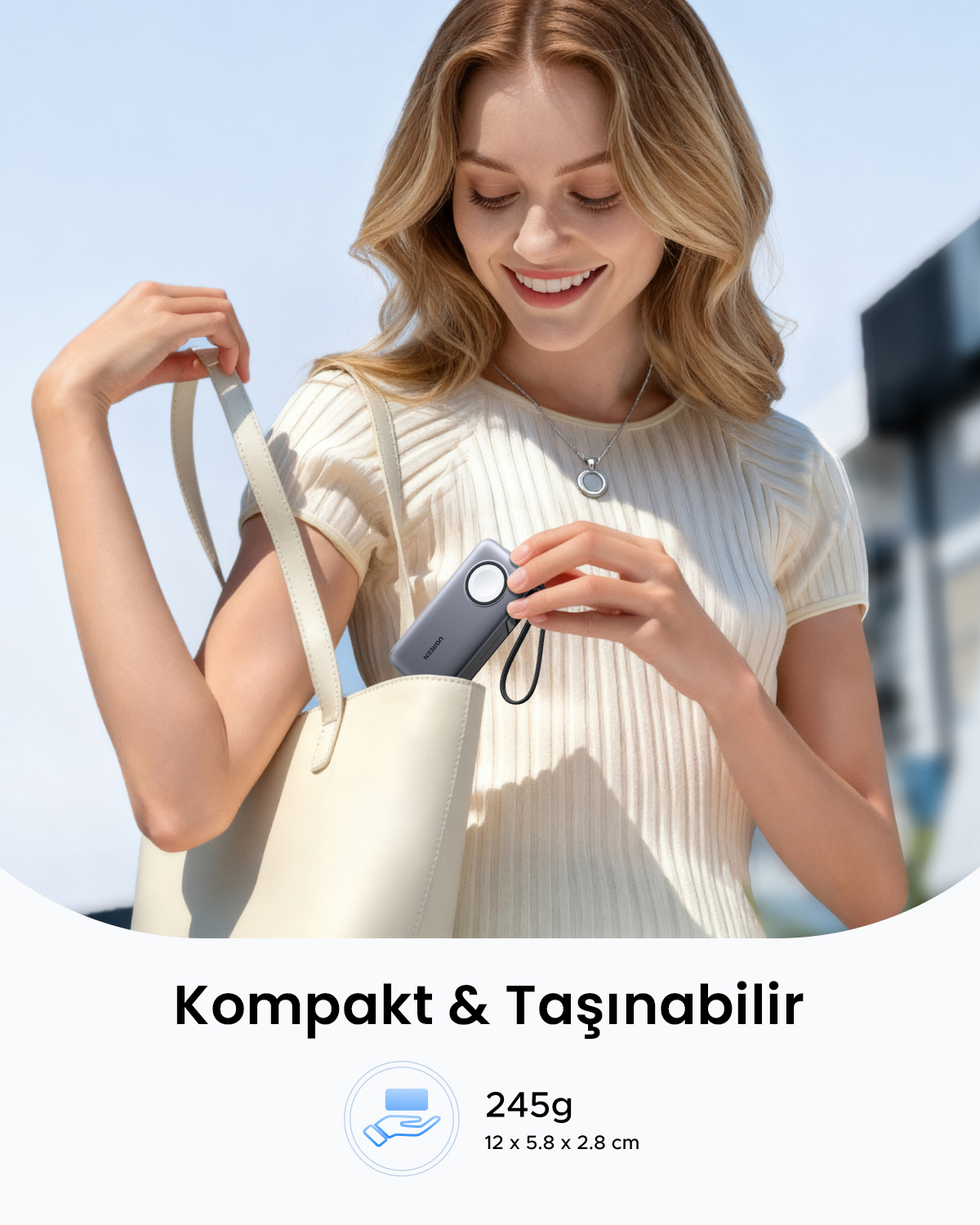 Kadın, krem rengi çantaya gri powerbank yerleştiriyor. Beyaz üst giyiyor.