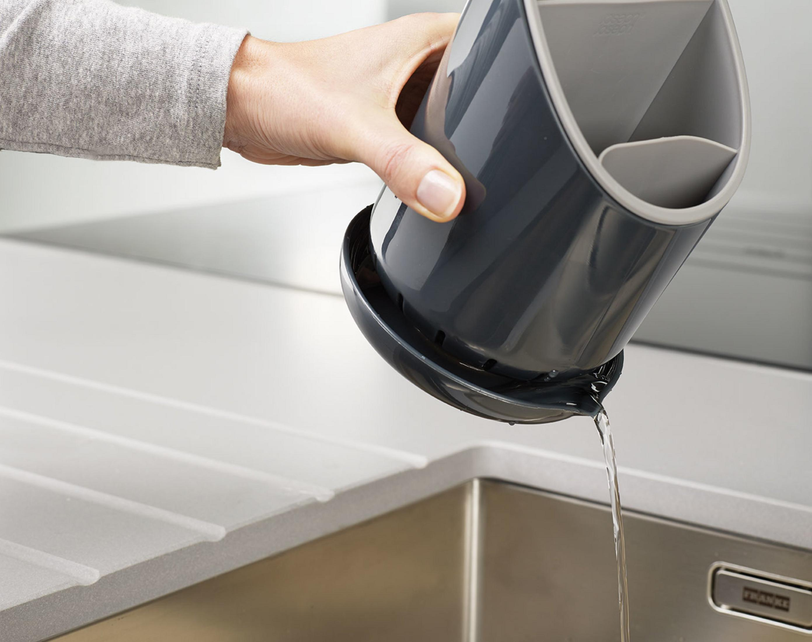 Una mano sostiene un escurridor oscuro sobre un fregadero; el agua gotea.
