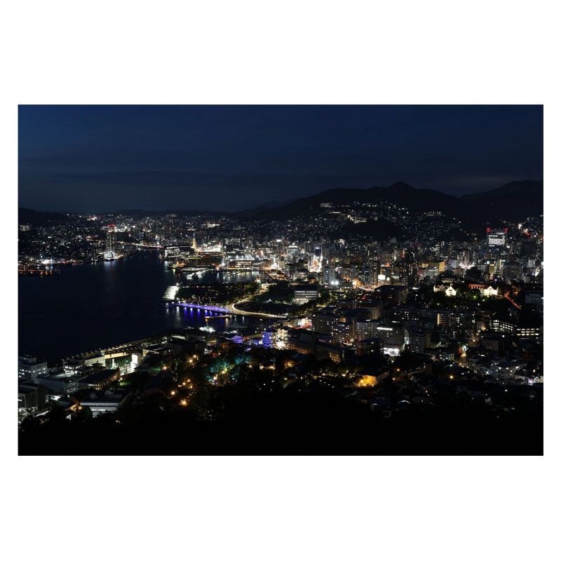 Eine Stadt bei Nacht mit Lichtern entlang der Küste und Hügeln im Hintergrund.