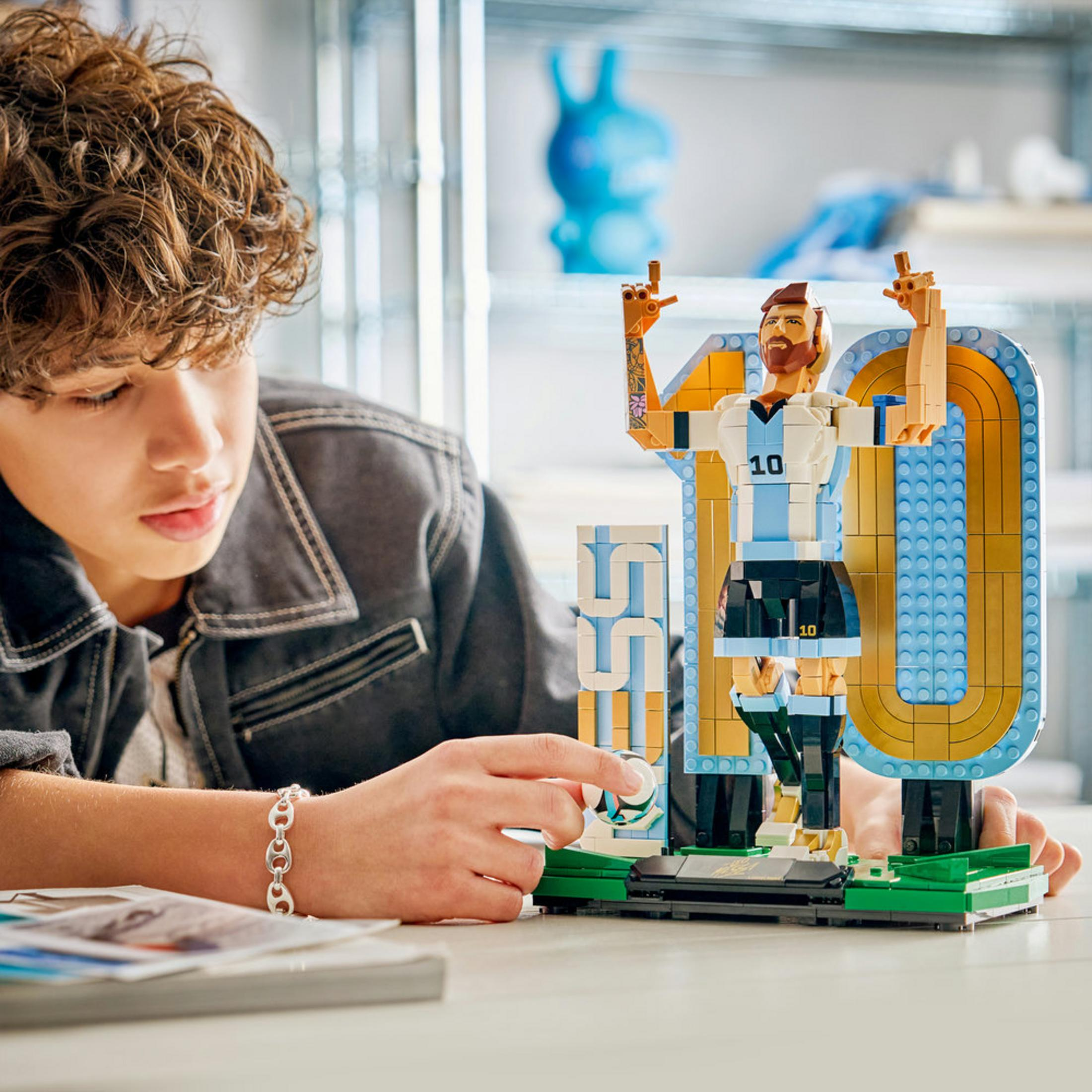 Un ragazzo costruisce una figura LEGO di Lionel Messi in divisa bianca e blu.
