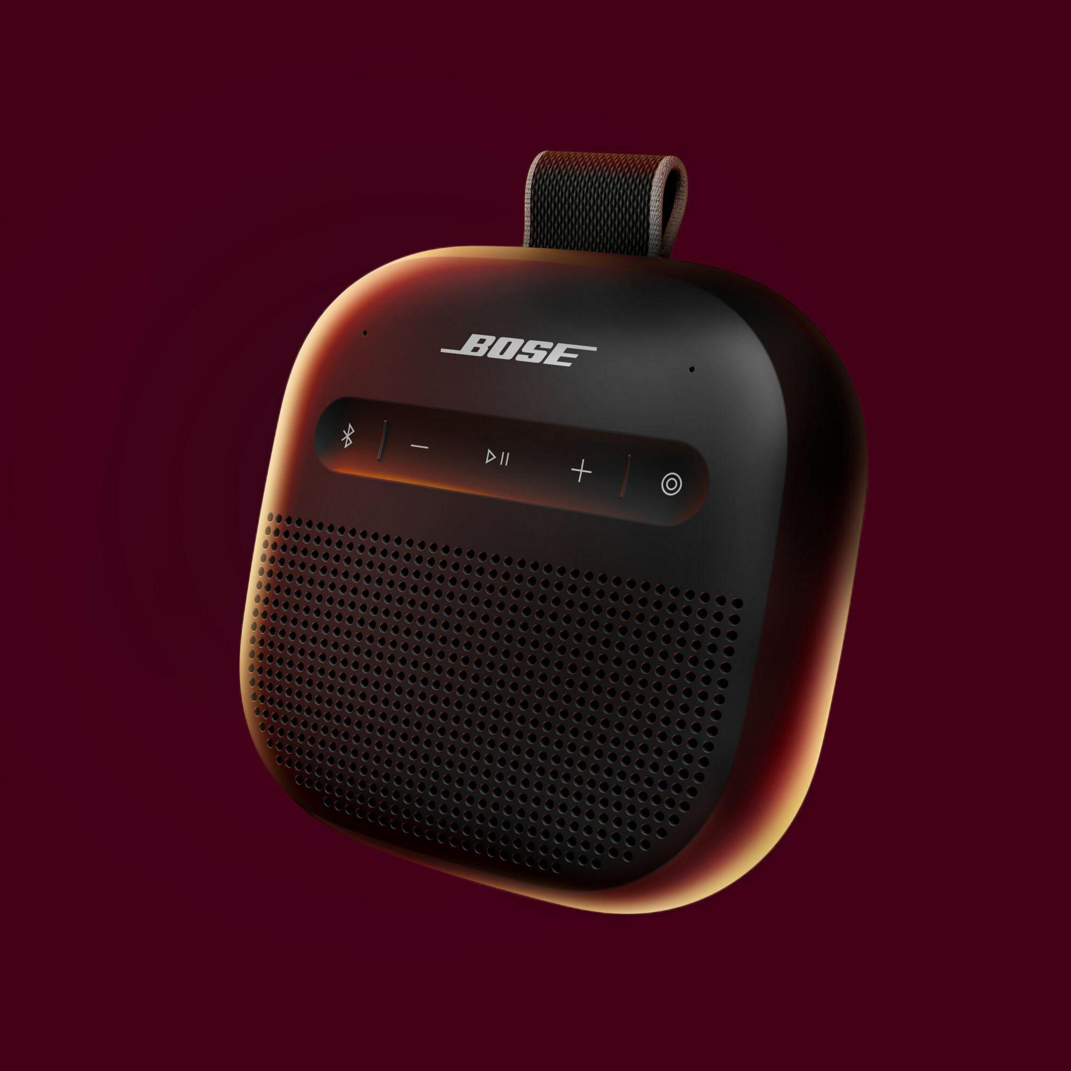Altavoz Bose negro con asa y controles sobre fondo rojo oscuro.