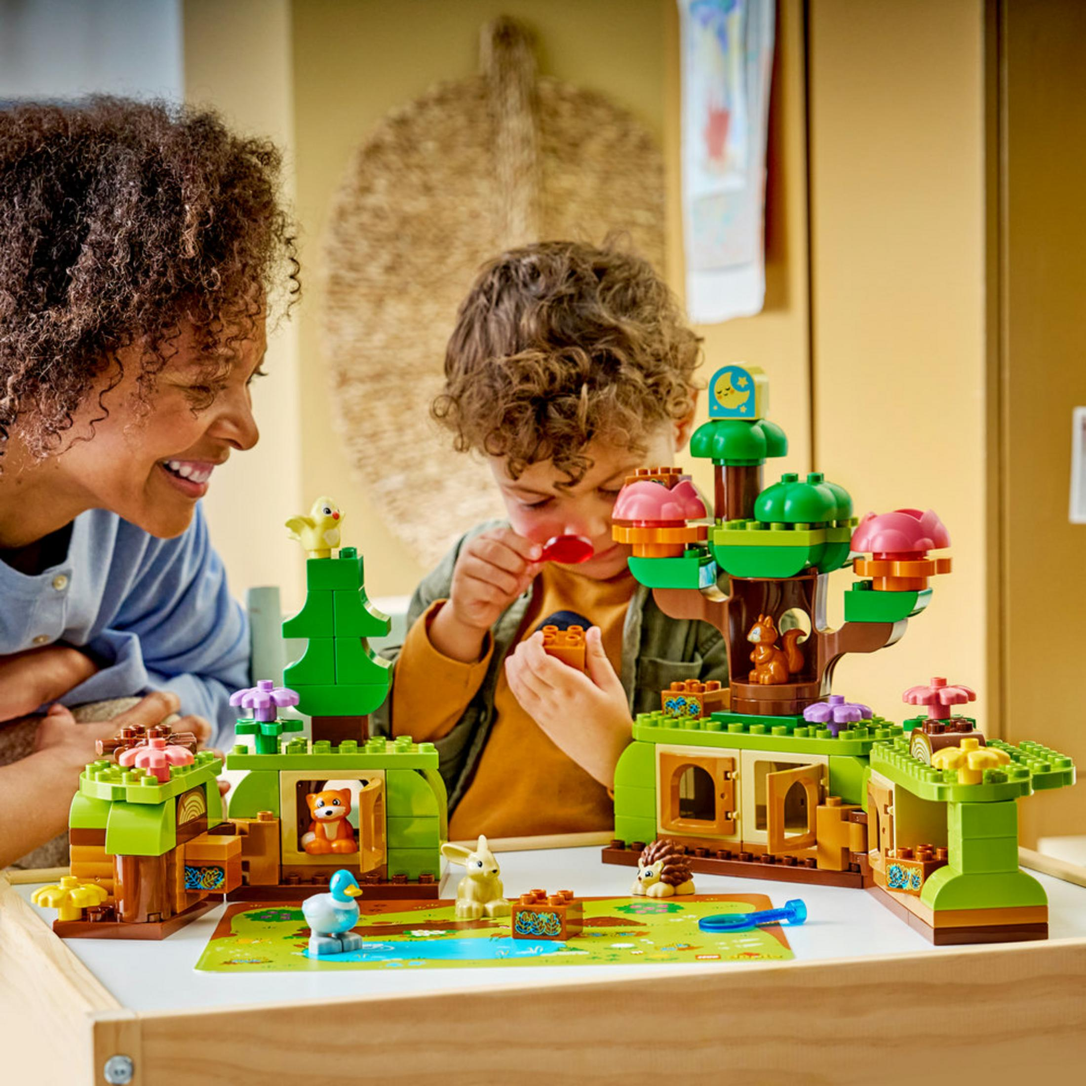 Donna e bambino giocano con figure di animali Duplo colorate e una casa sull'albero.