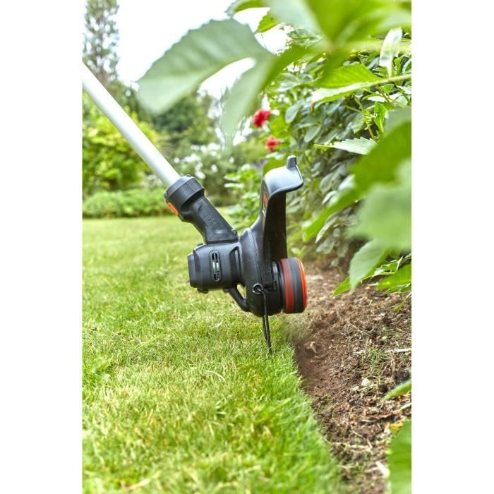 Una cortadora de césped corta el borde del césped cerca de las plantas.