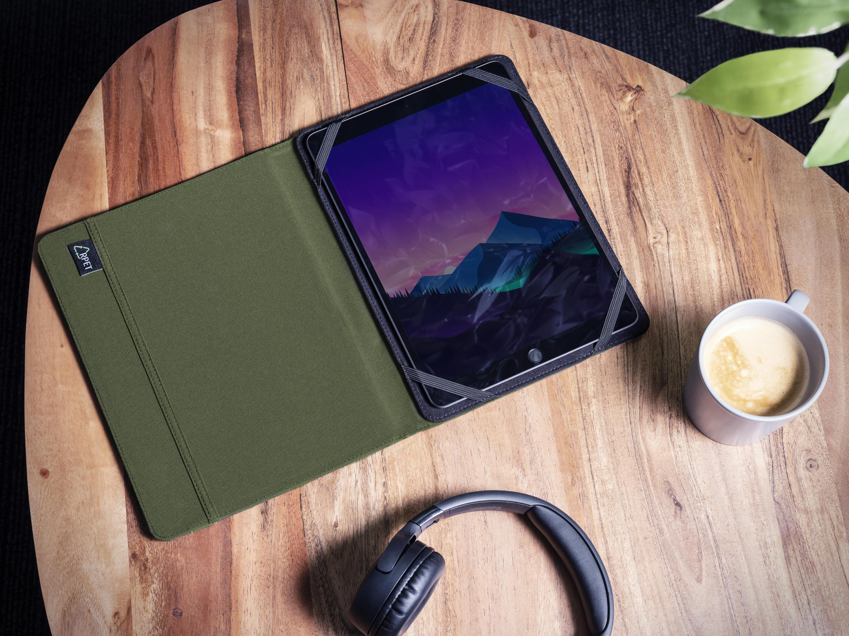 Una tableta en una funda verde con auriculares y una taza de café sobre una mesa de madera.