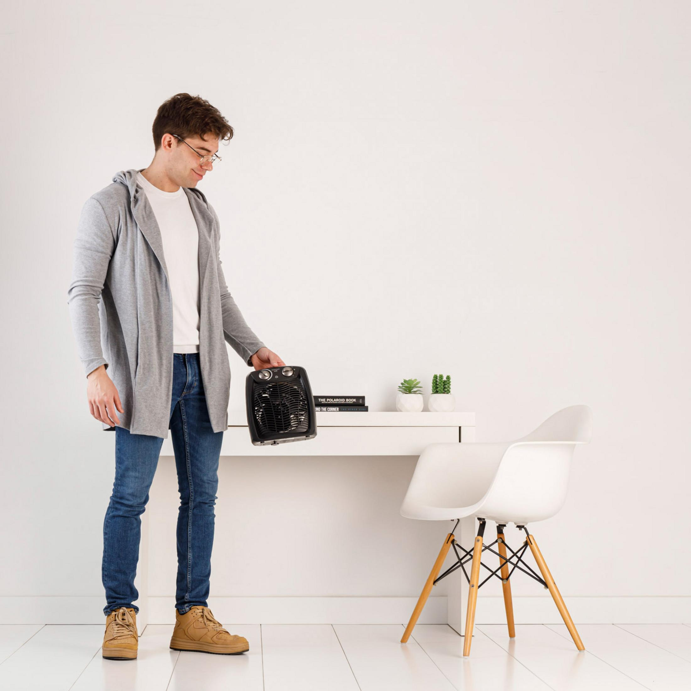 Uomo con termoventilatore portatile in stanza minimalista con scrivania e sedia.