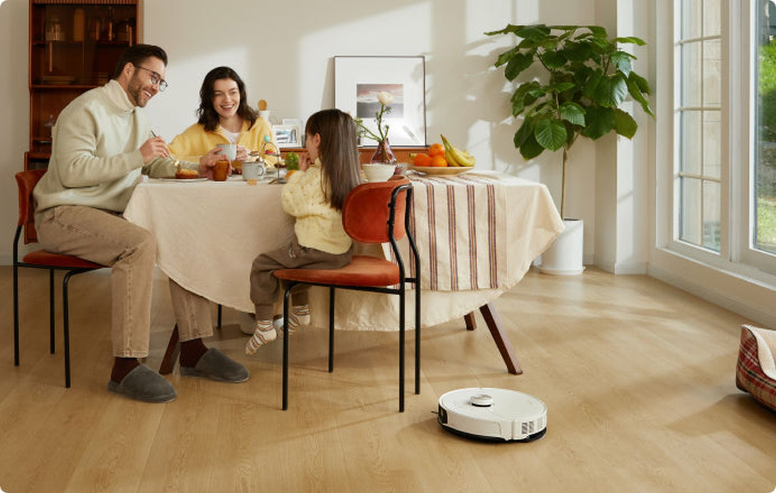 Famiglia mangia a tavola, robot aspirapolvere pulisce il pavimento.