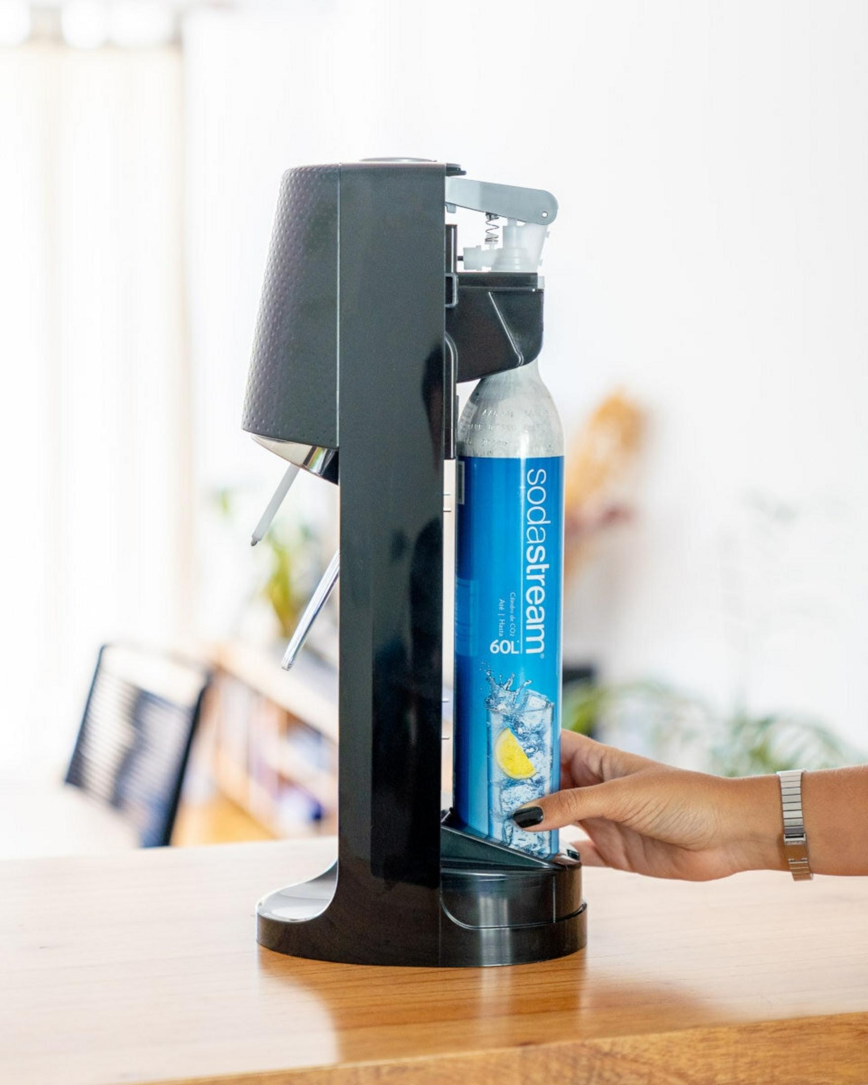 Una mano inserisce una bottiglia blu Sodastream in un carbonatore d'acqua nero.