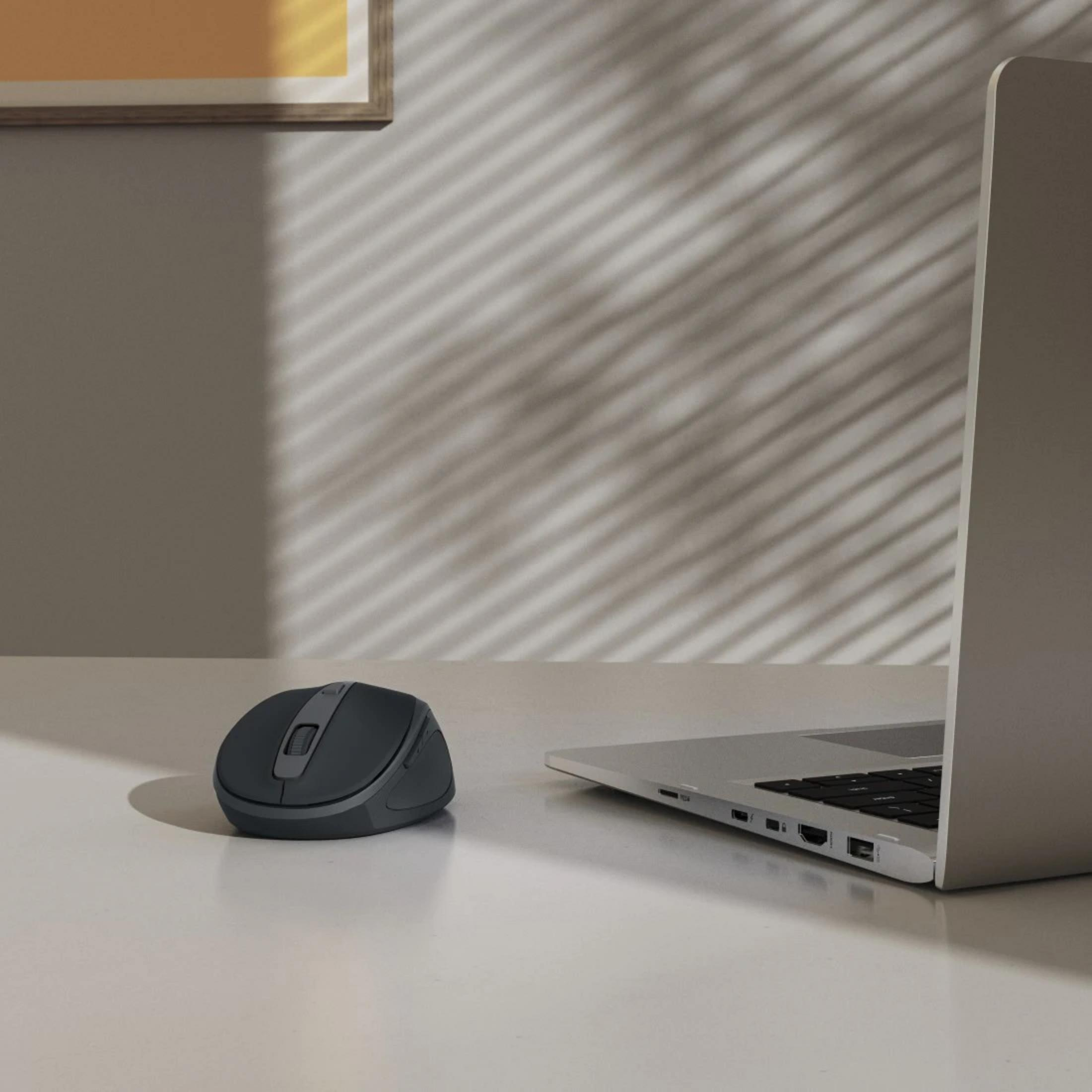 Un mouse scuro e un laptop su una scrivania bianca, con un motivo a ombre sul muro.