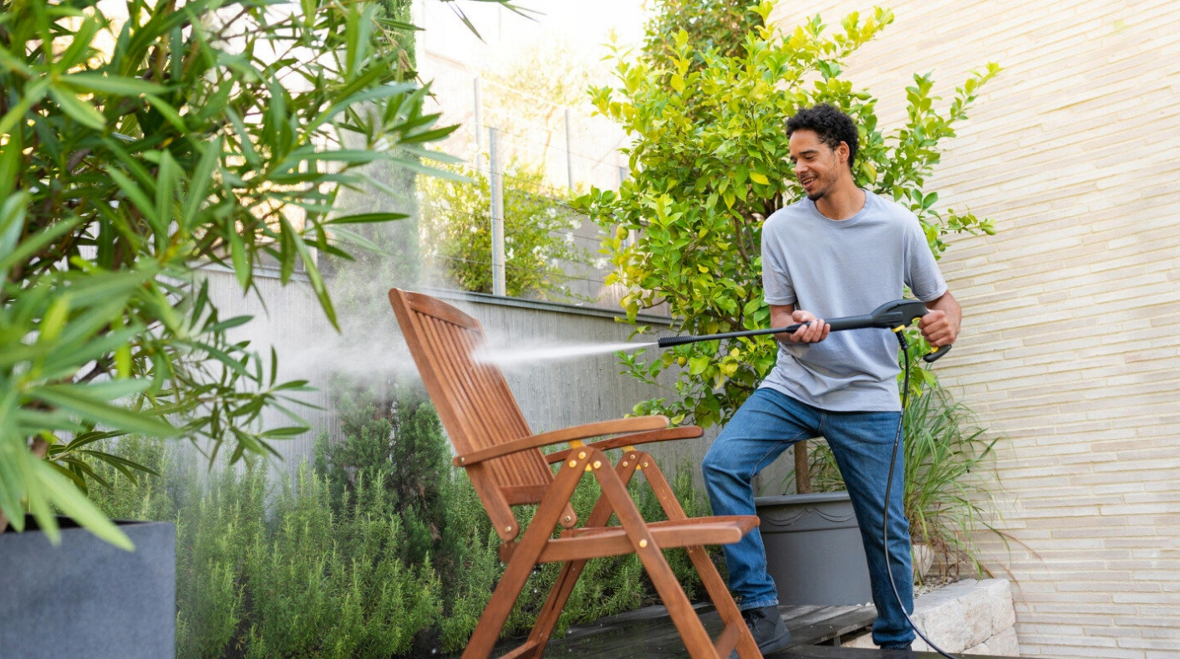Uomo pulisce sedia in legno con idropulitrice in giardino.
