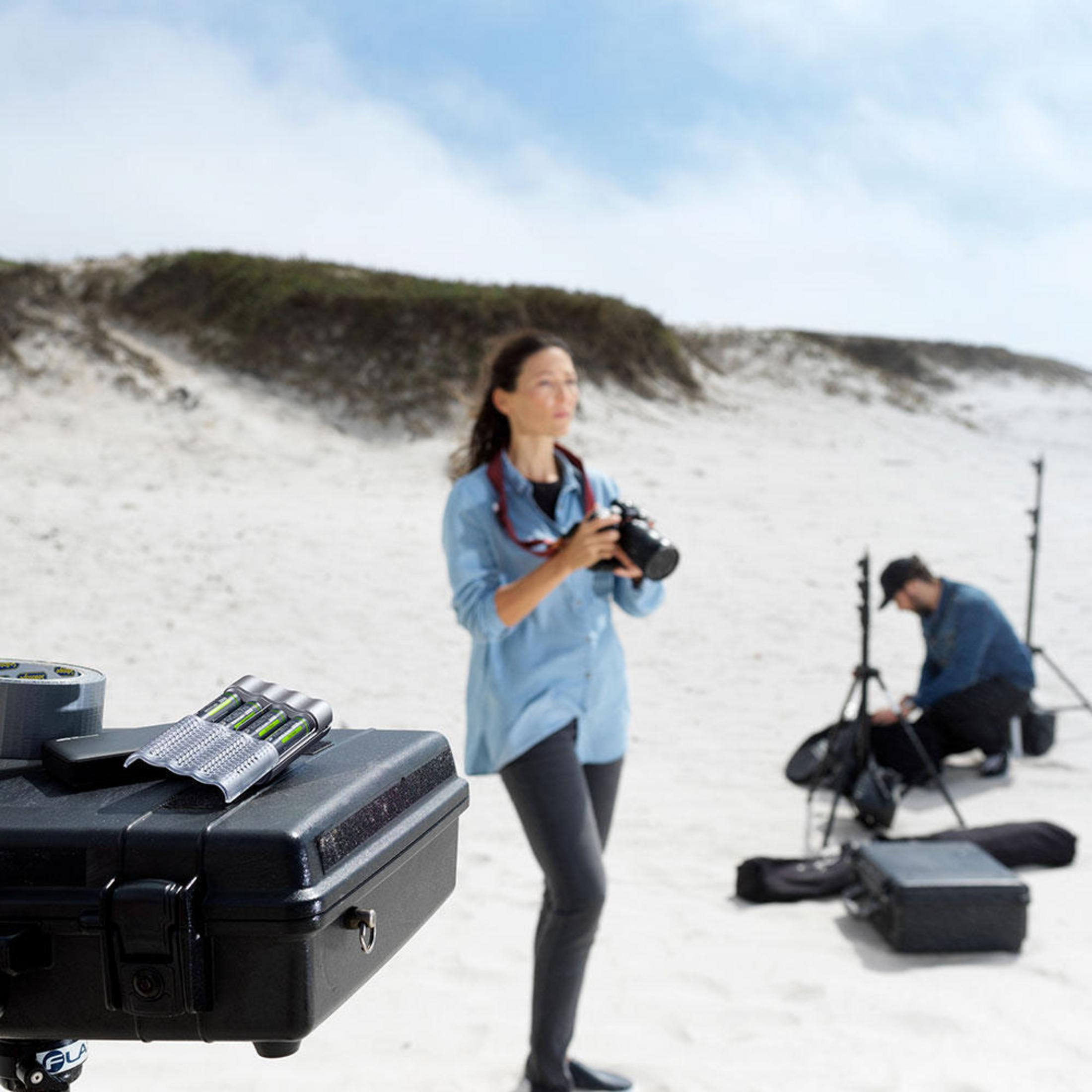 Su una spiaggia sabbiosa, una donna tiene una macchina fotografica. Attrezzatura in primo piano.