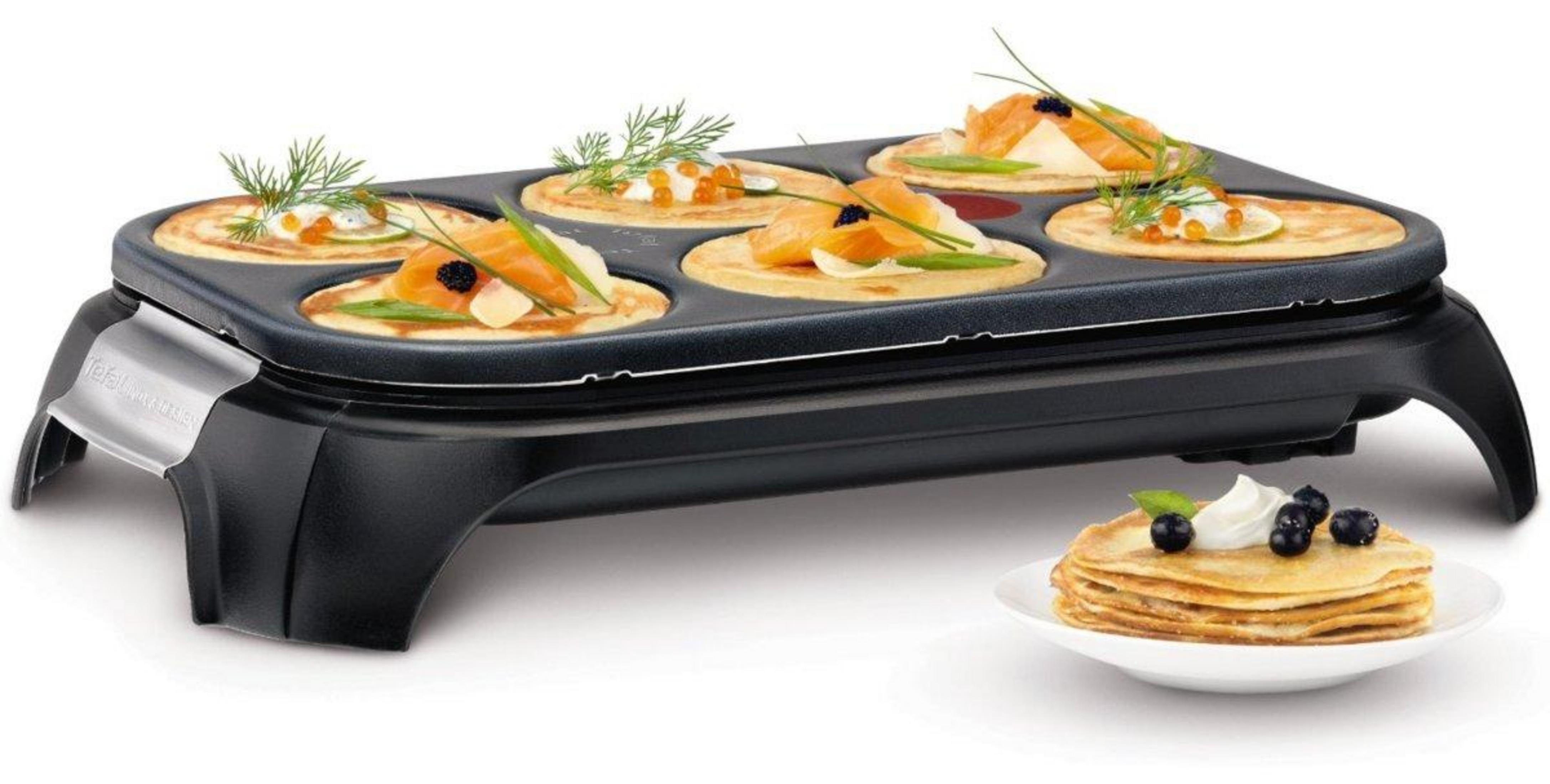 Una piastra per crepes elettrica con sei crepes ripiene e una pila di crepes accanto.
