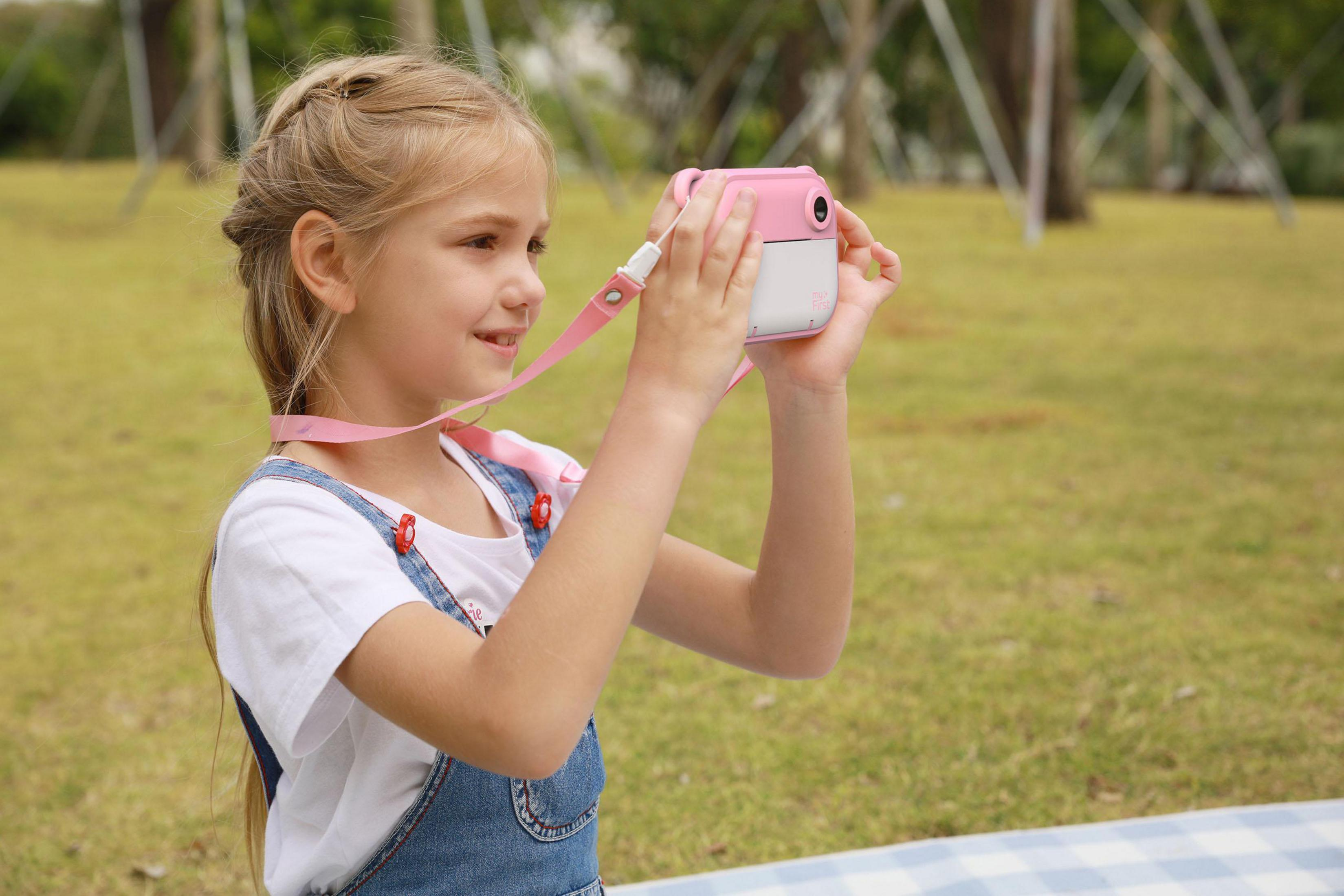 Una niña rubia sostiene una cámara rosa y sonríe.
