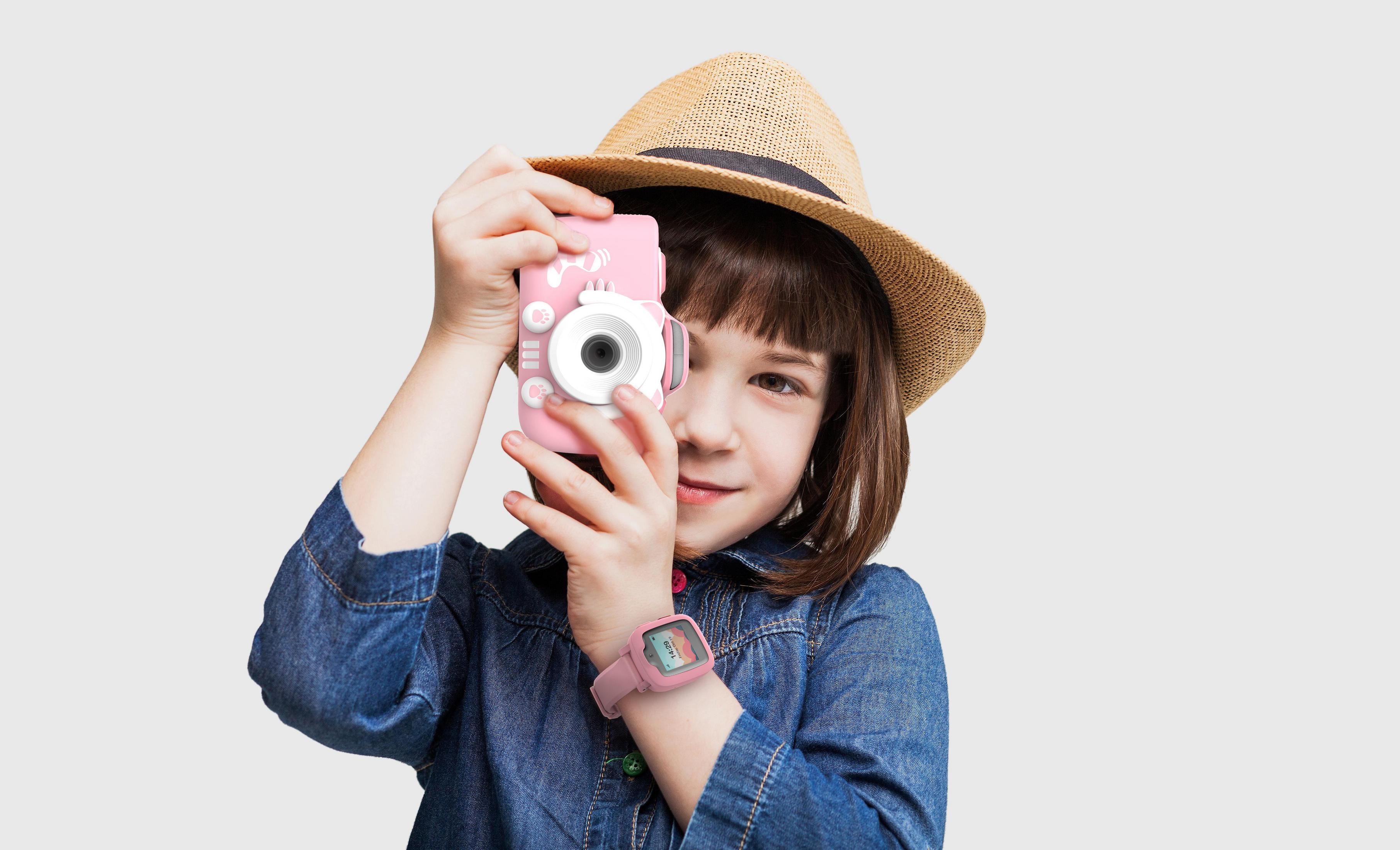 Una bambina con cappello tiene una fotocamera rosa davanti al viso.