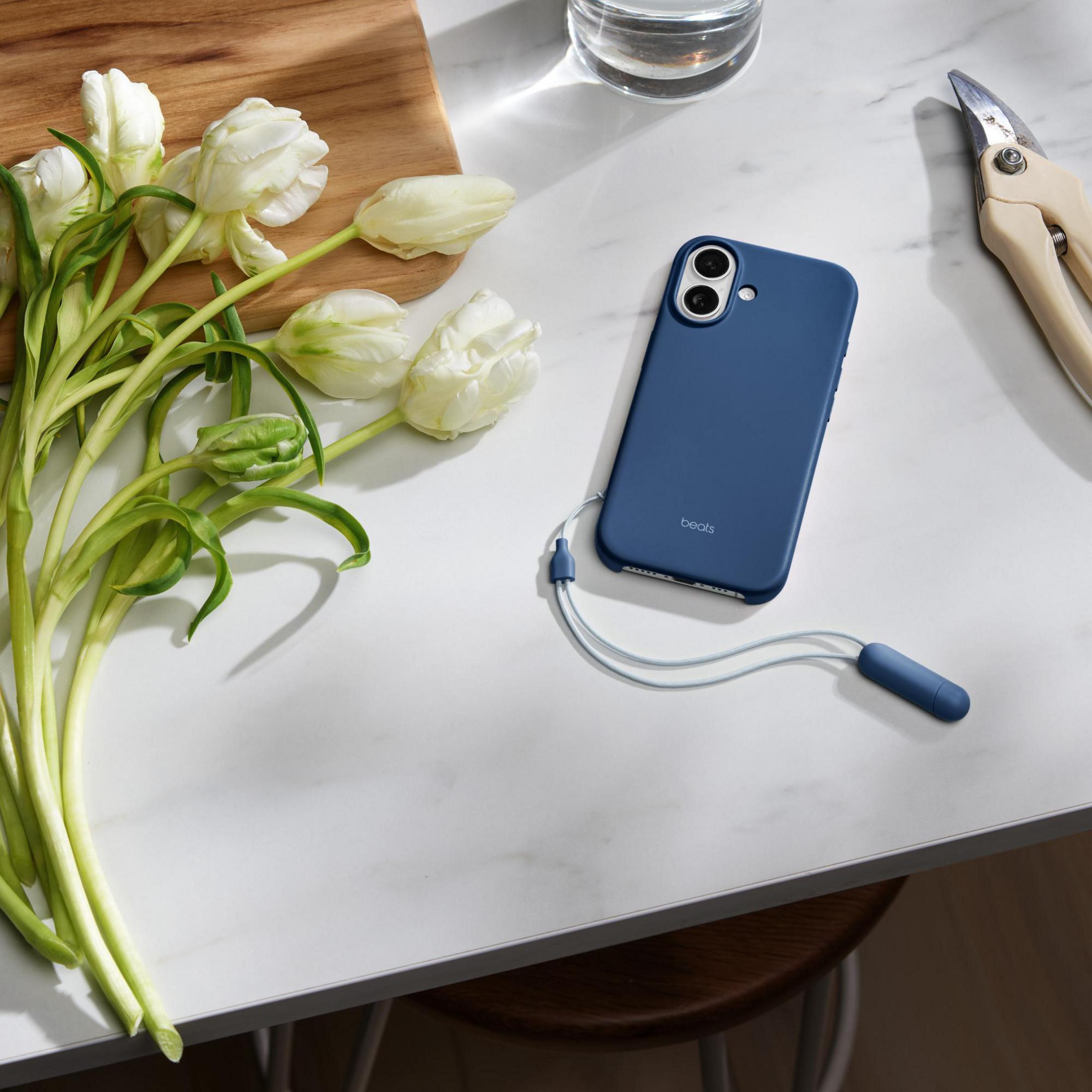 Tulipani bianchi, custodia blu per telefono e forbici su marmo bianco.