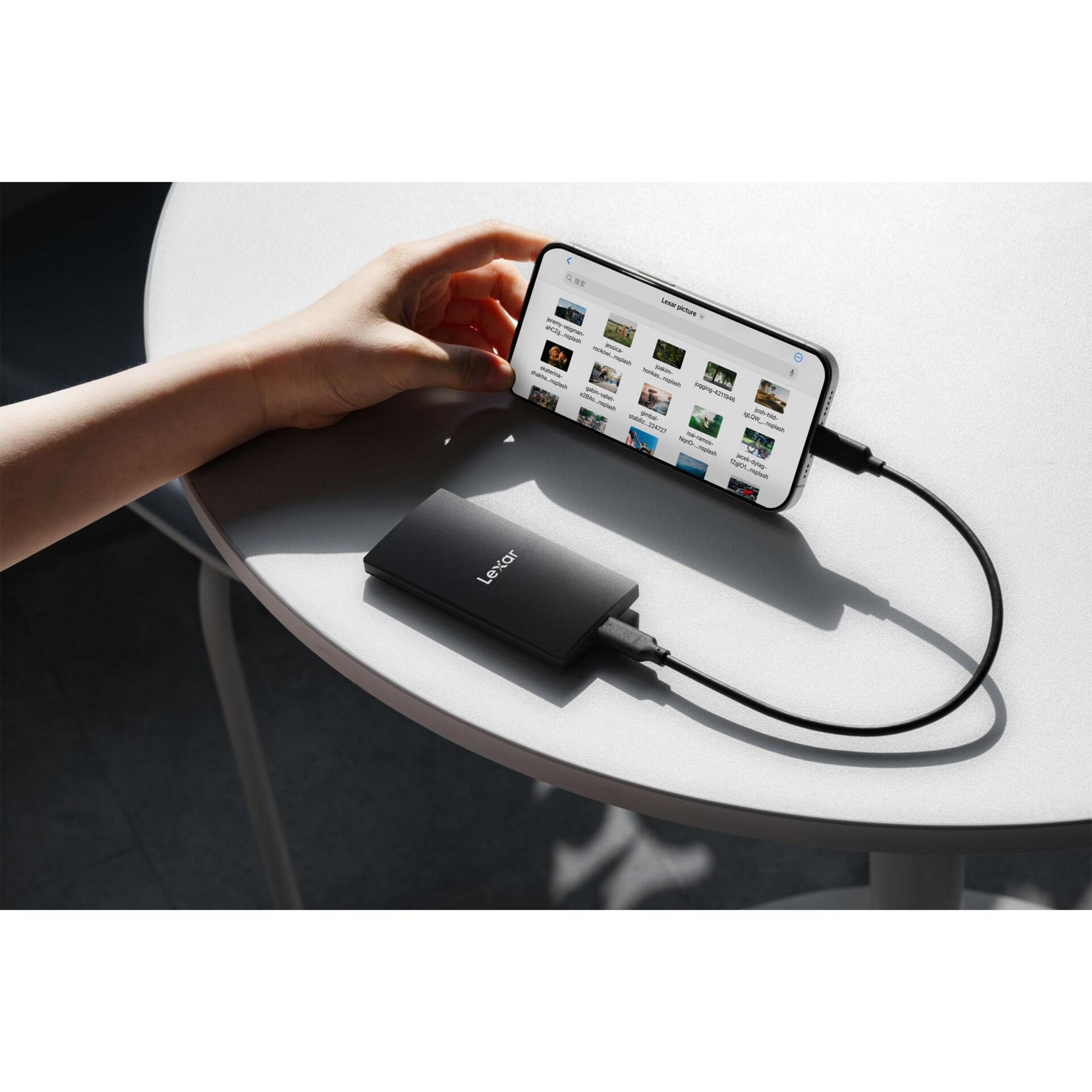 Una mano tiene uno smartphone collegato a un hard disk esterno Lexar.