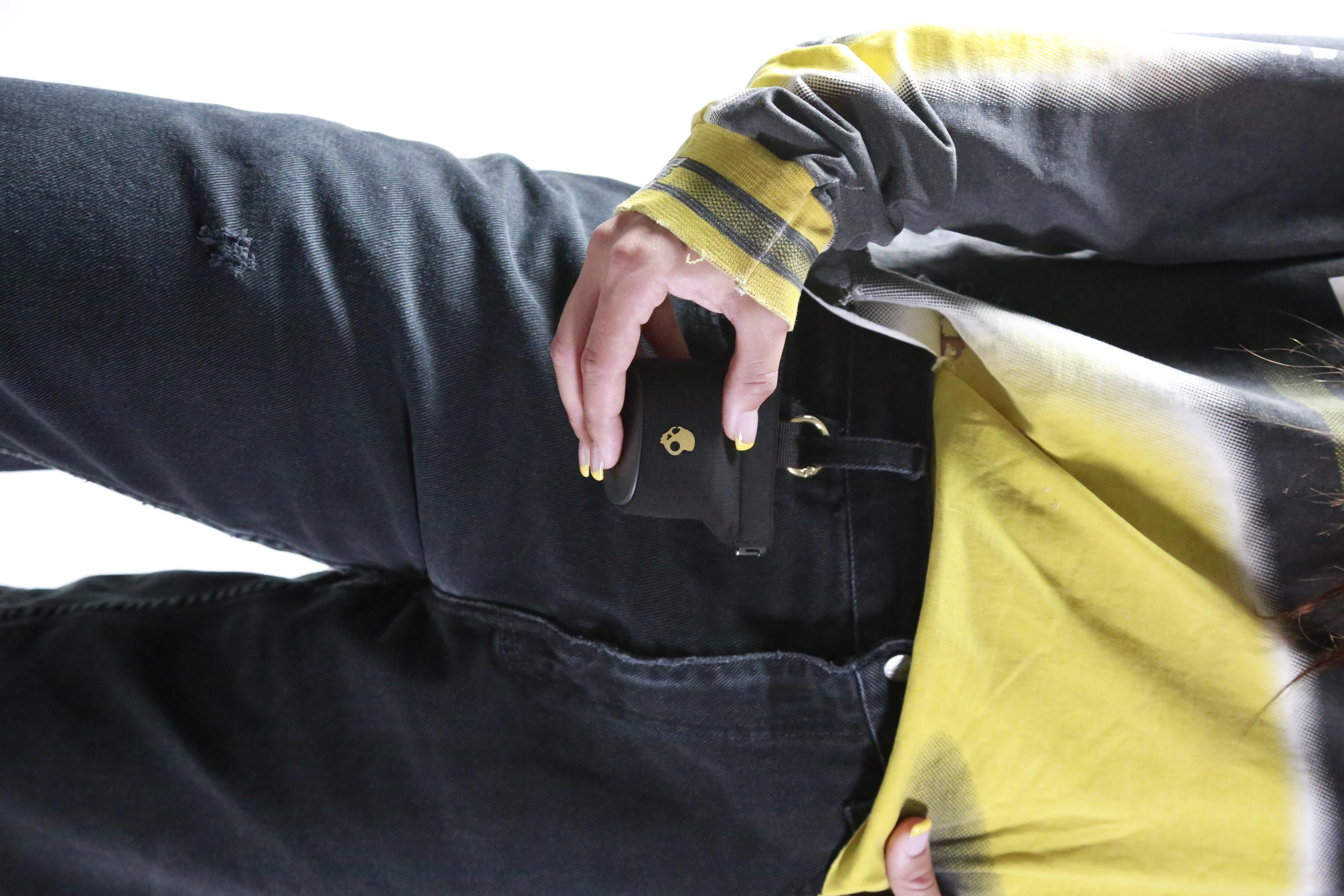 Una mano con smalto giallo tiene una piccola pochette nera con emblema a teschio.