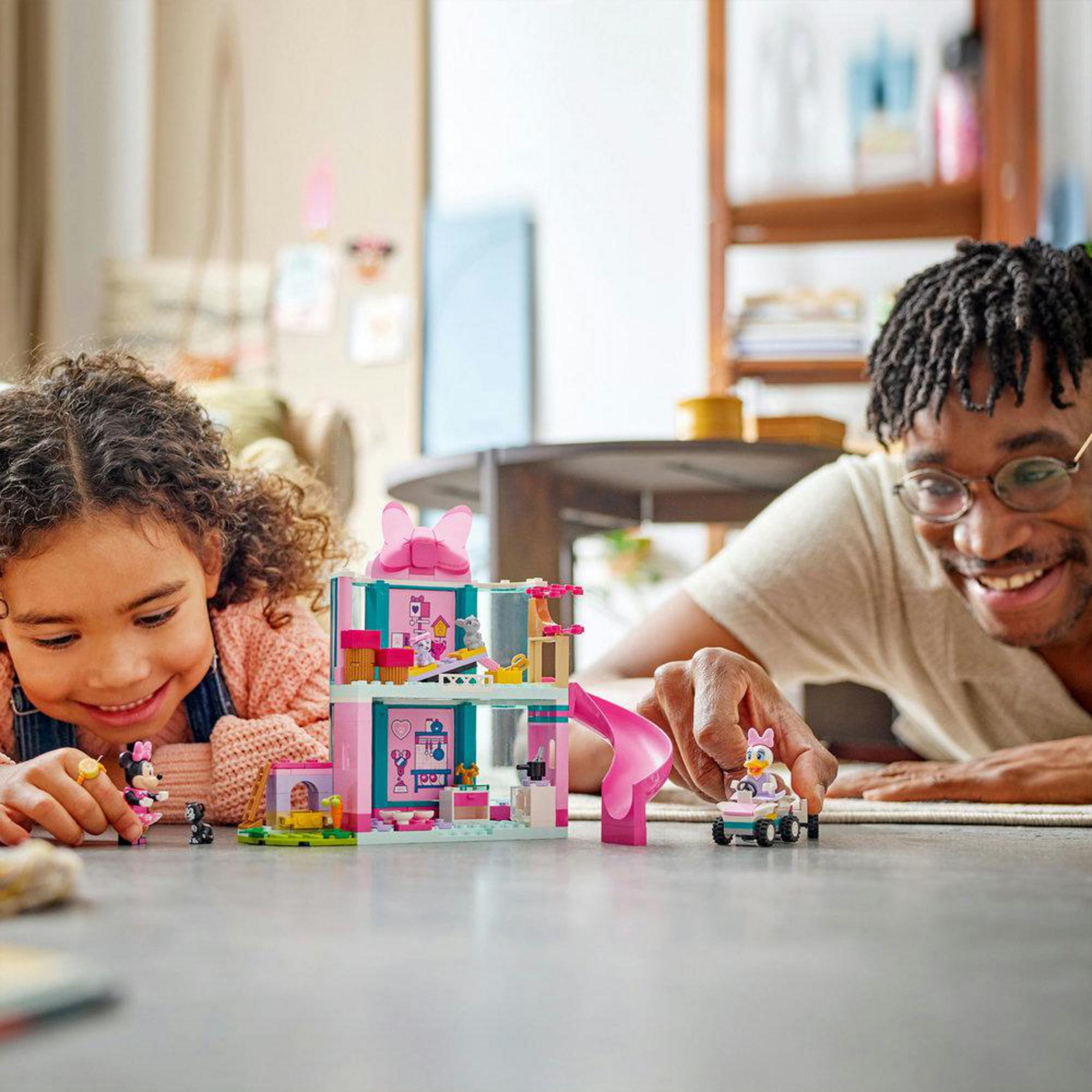 Un hombre y un niño construyen una casa de juguete rosa con figuras.