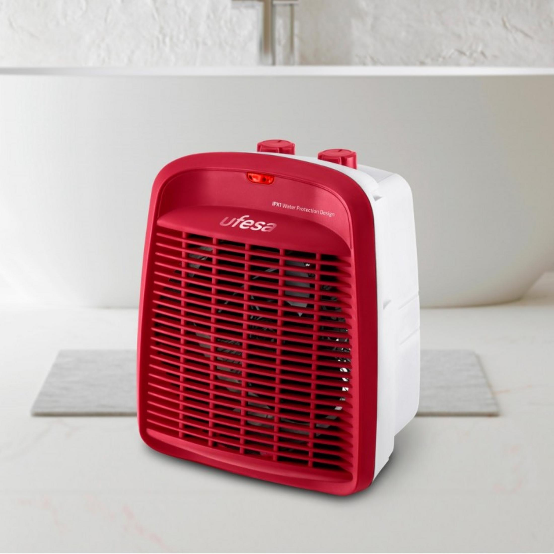 Un calefactor de ventilador rojo y blanco con rejilla se posa sobre una superficie clara.