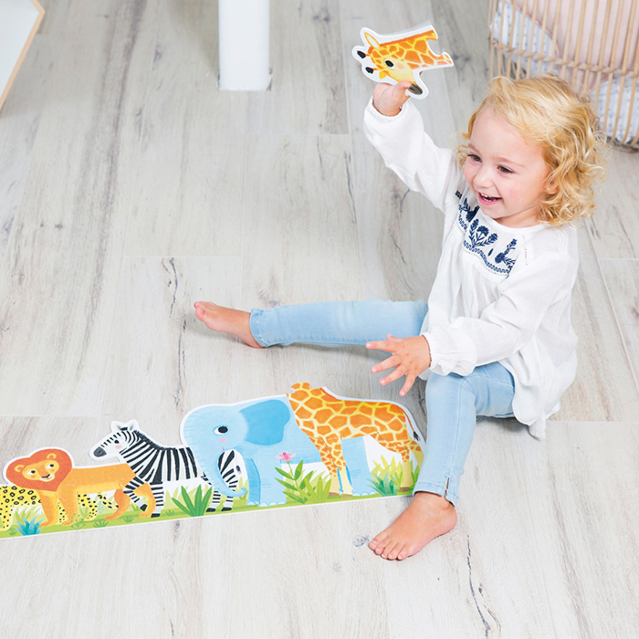 Een jong meisje speelt met een girafspeeltje op een houten vloer.