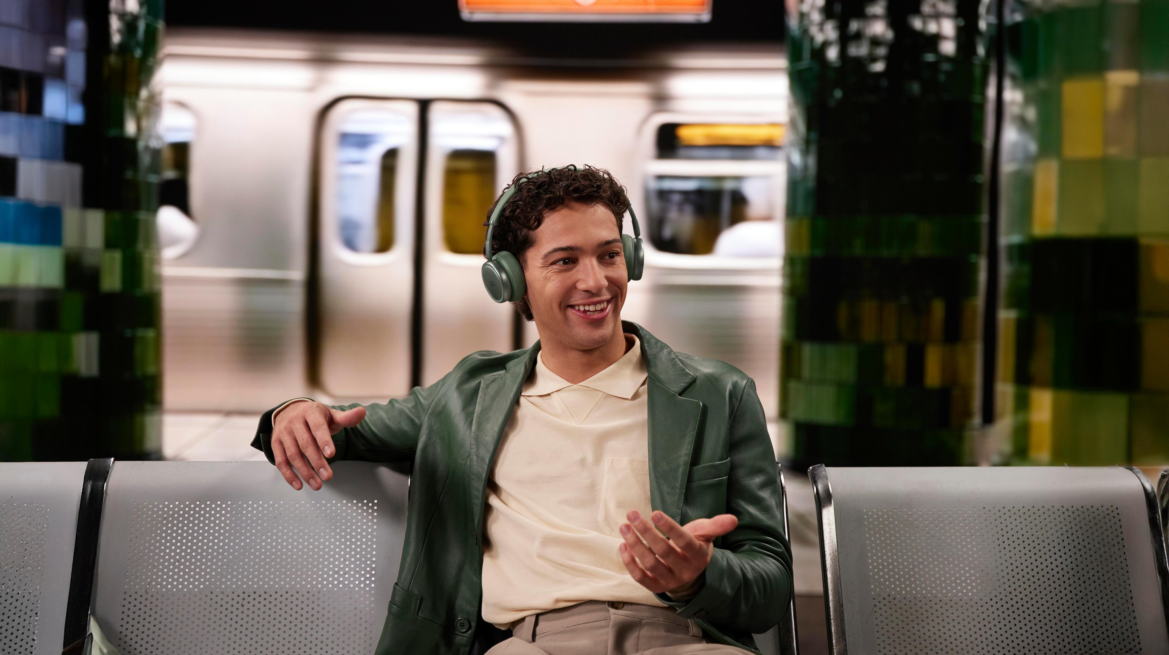 Un uomo con le cuffie seduto su una panchina della metropolitana, sorride.