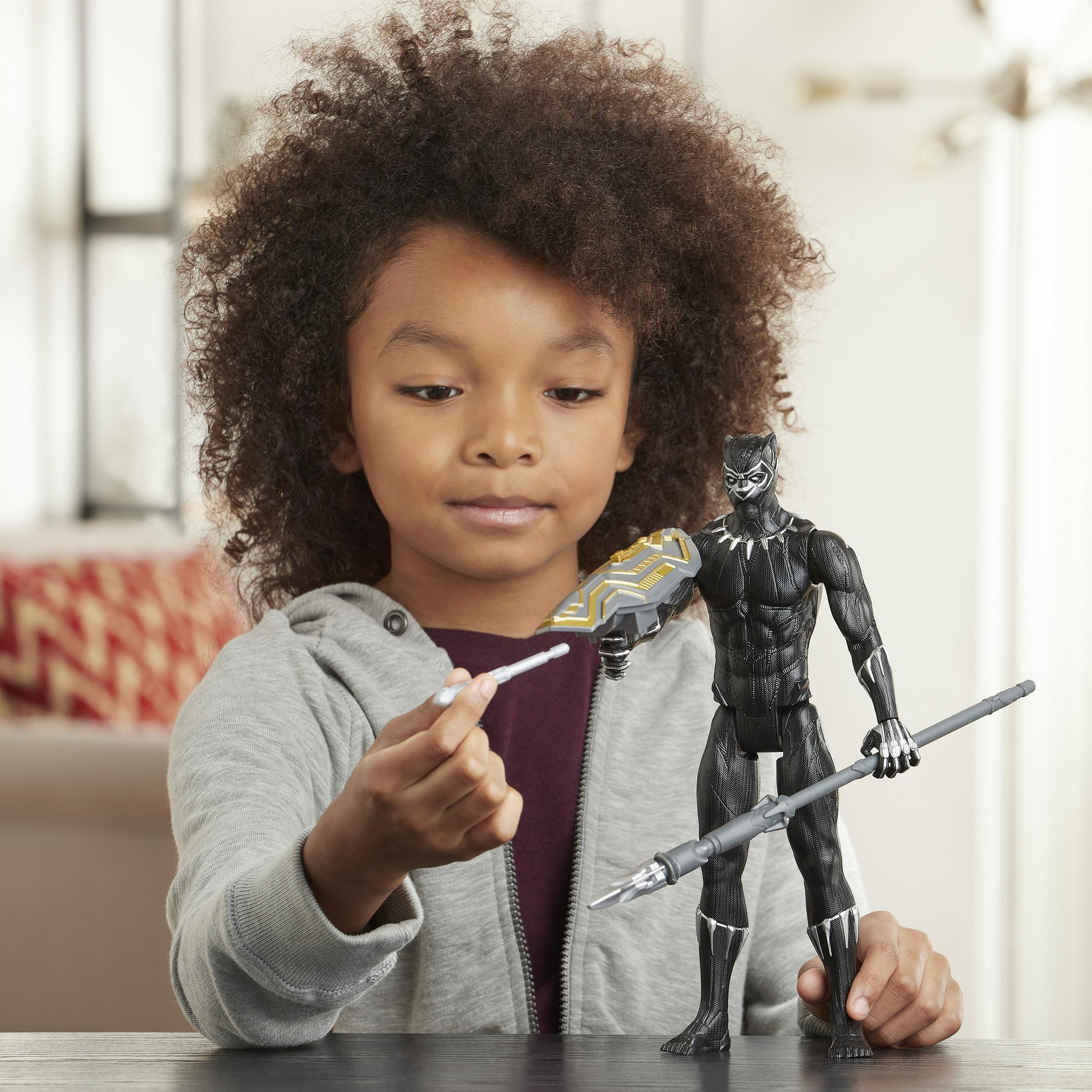 Un bambino con capelli ricci tiene una figura di Black Panther con scudo e lancia.