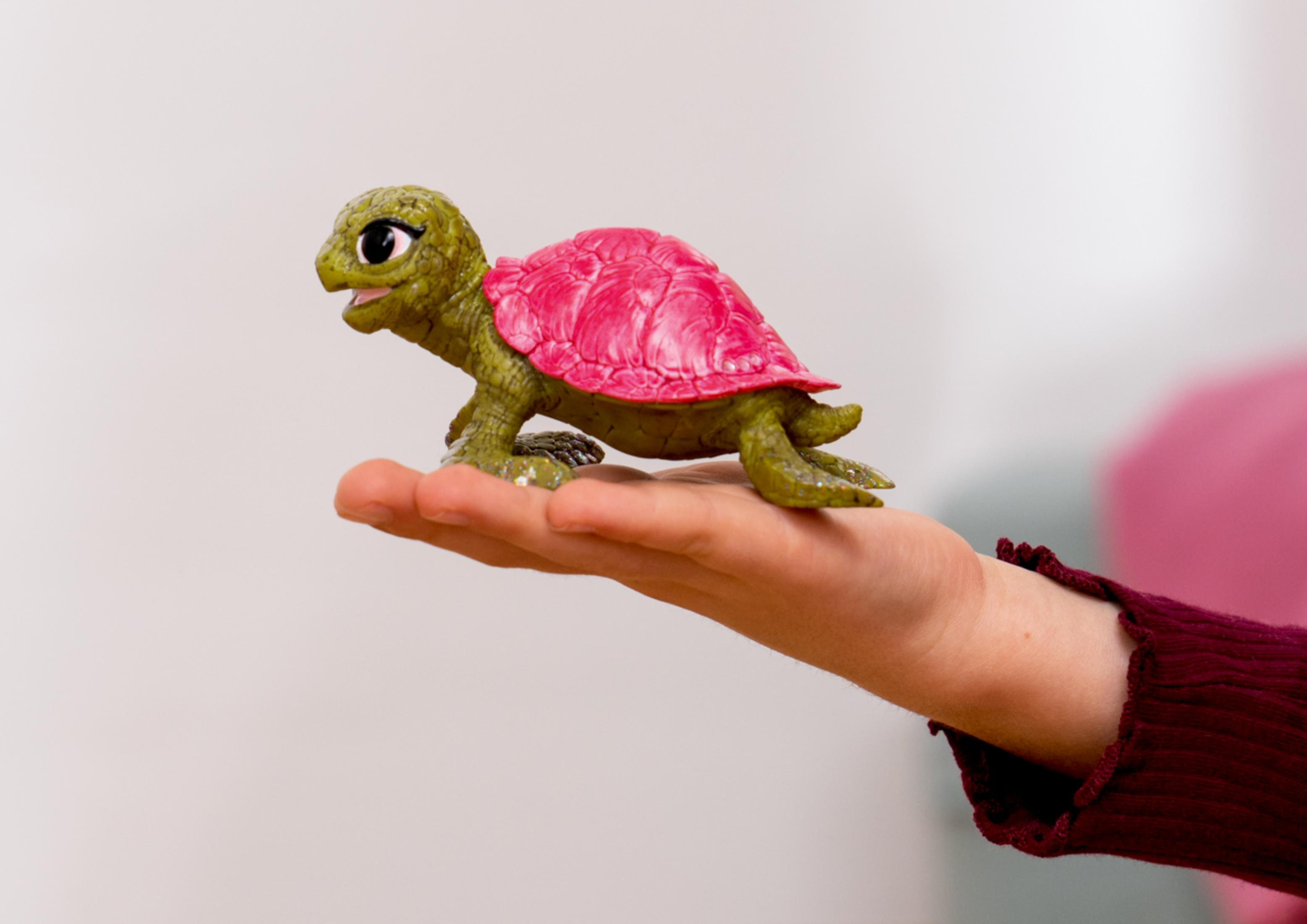 Una tartaruga giocattolo verde con guscio rosa riposa su una mano.