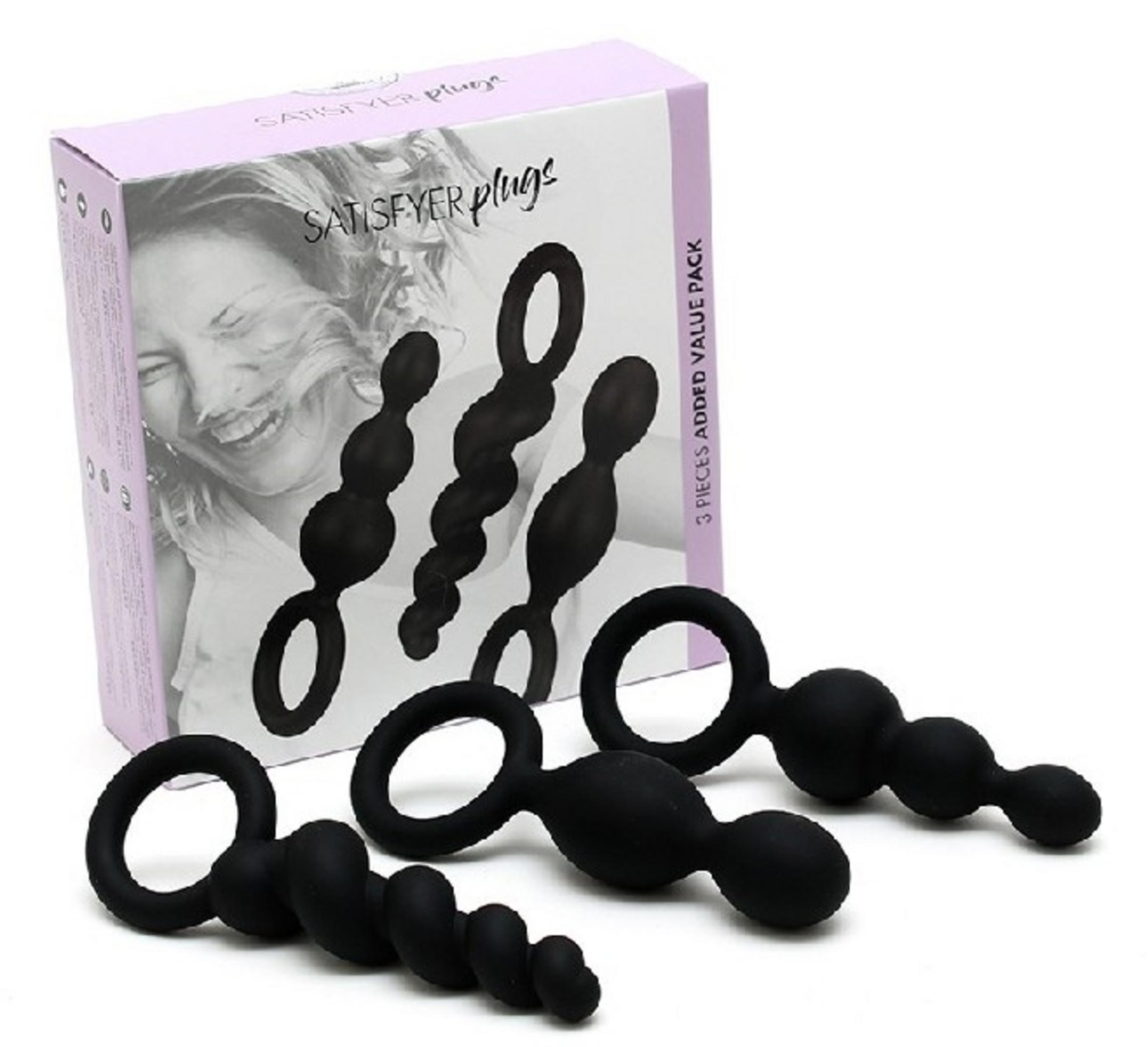 Drei schwarze, texturierte Plug-Toys mit Ringen auf weißem Grund neben einer Box.
