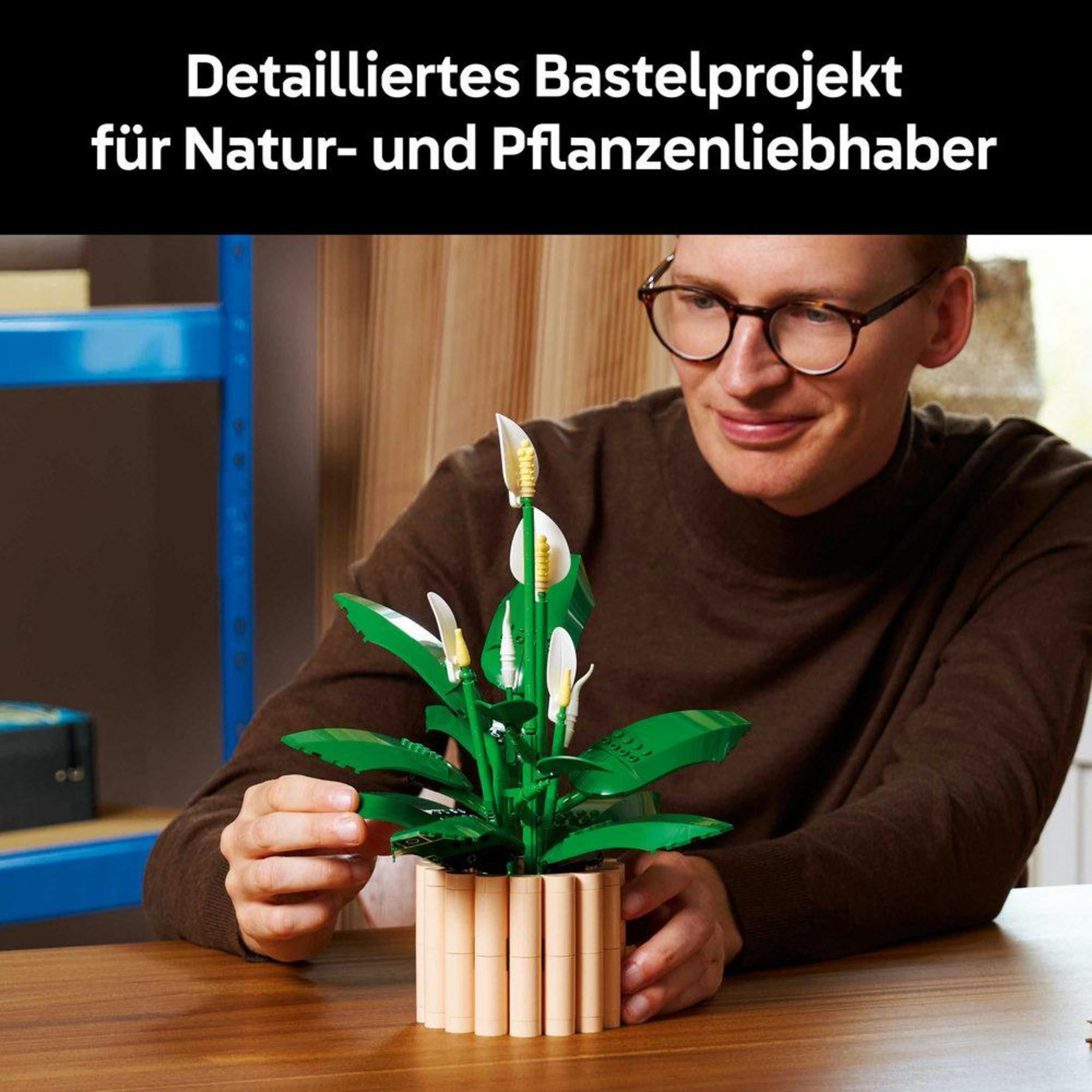 Hombre con gafas construye una planta verde de Lego en una maceta sobre una mesa de madera.