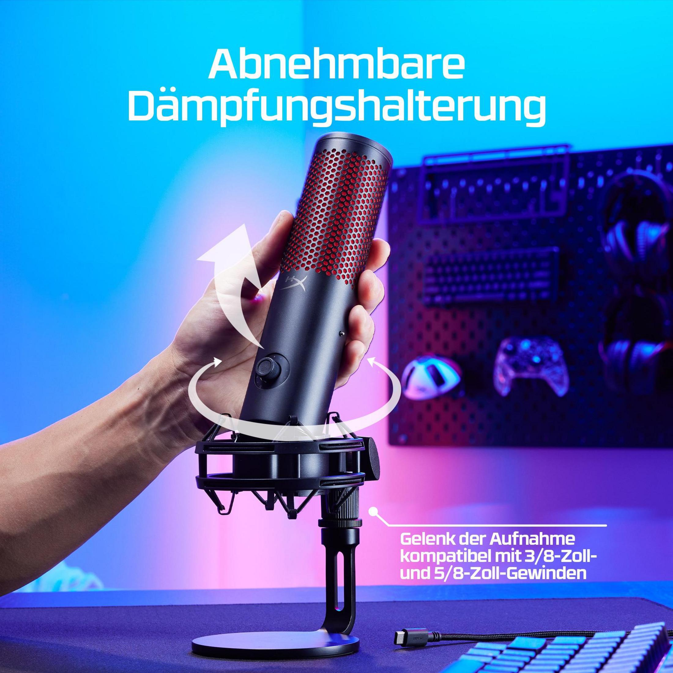 Une main tient un microphone noir à grille rouge. Accessoires de jeu en arrière-plan.