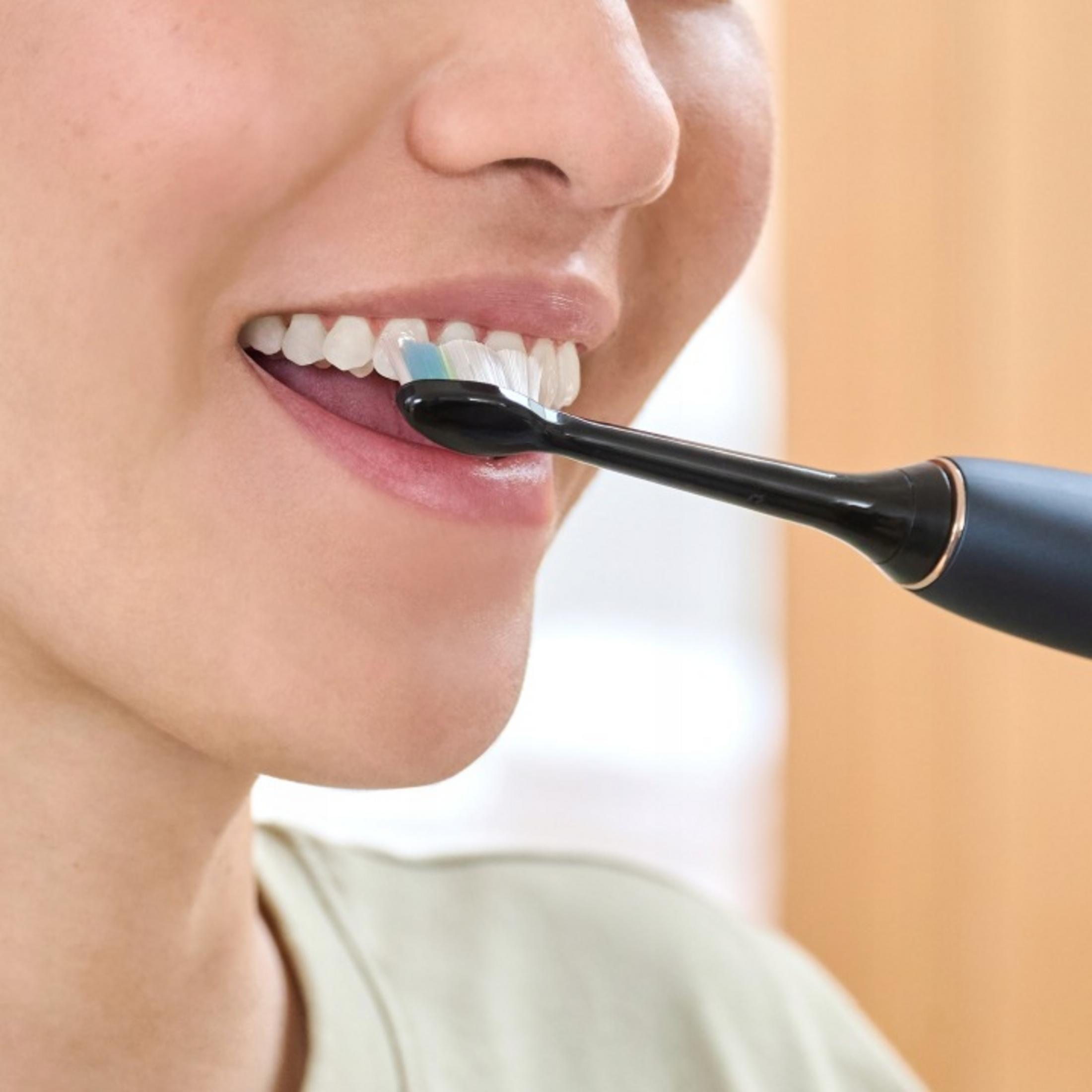 Primer plano de una persona cepillándose los dientes con un cepillo eléctrico negro.
