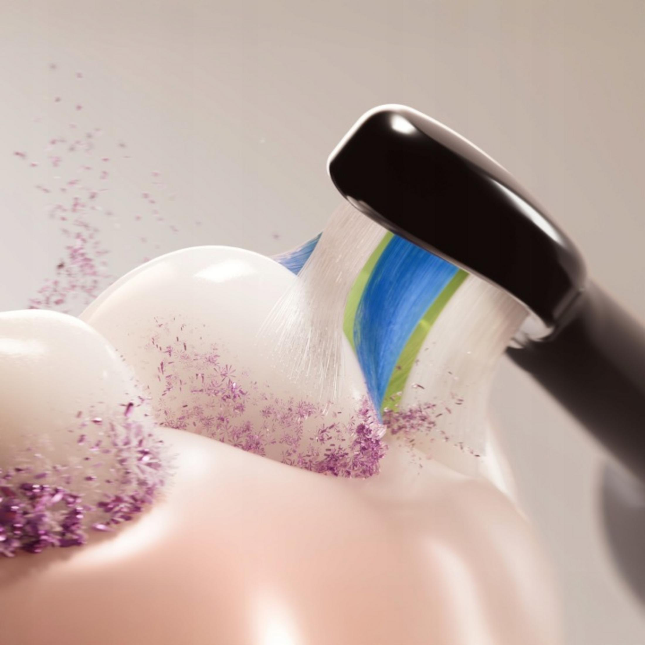 Un cepillo de dientes negro limpia dientes blancos con partículas púrpuras.