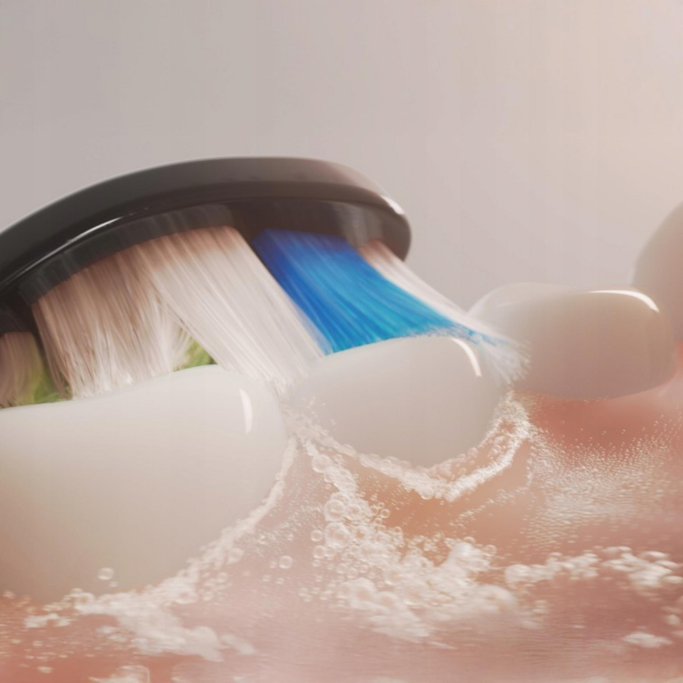 Un cepillo de dientes eléctrico con cerdas azules y blancas limpia dientes blancos con agua.
