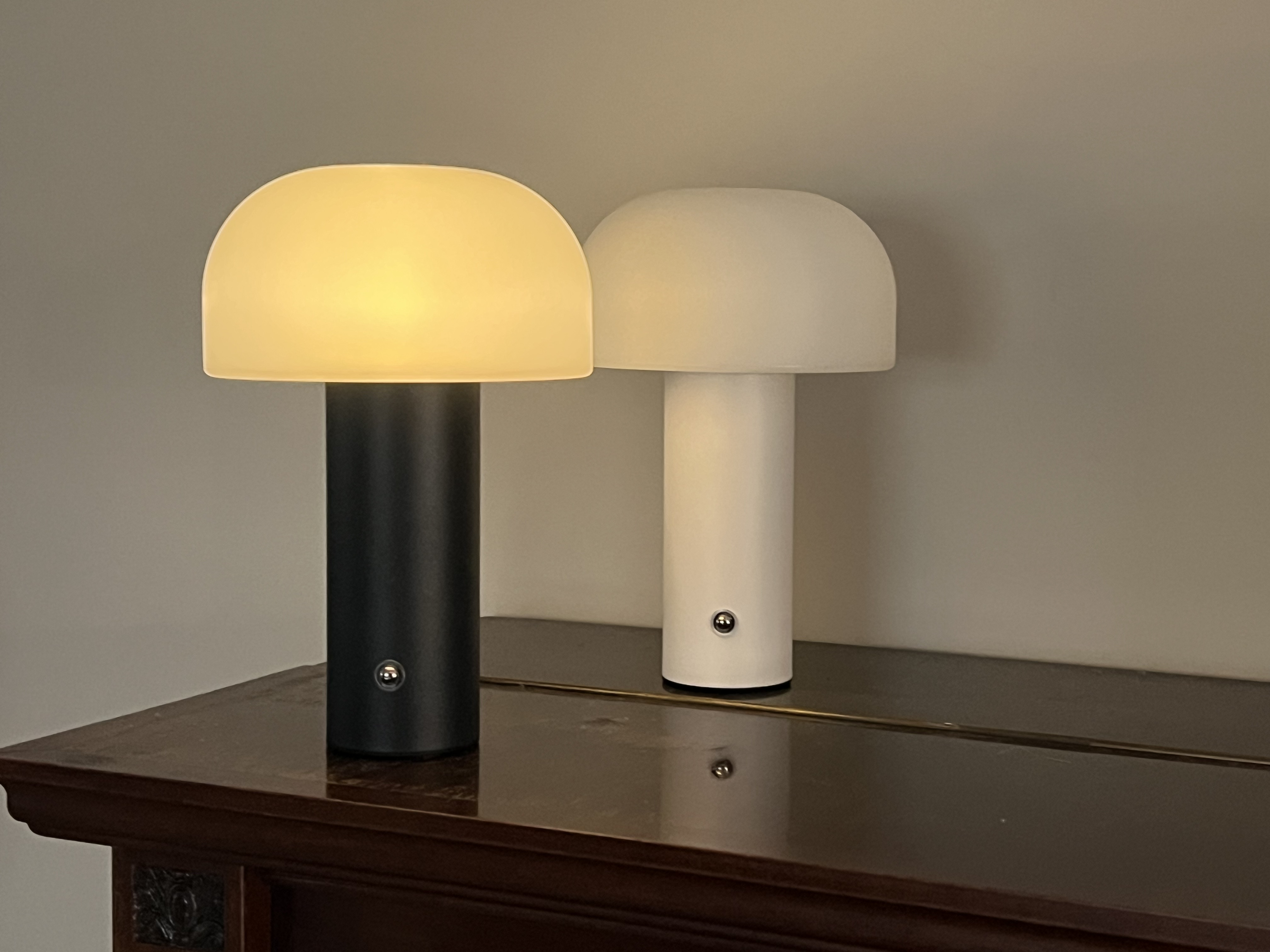 Zwei Pilzförmige Lampen, eine schwarz, eine weiß, auf einem dunklen Tisch.