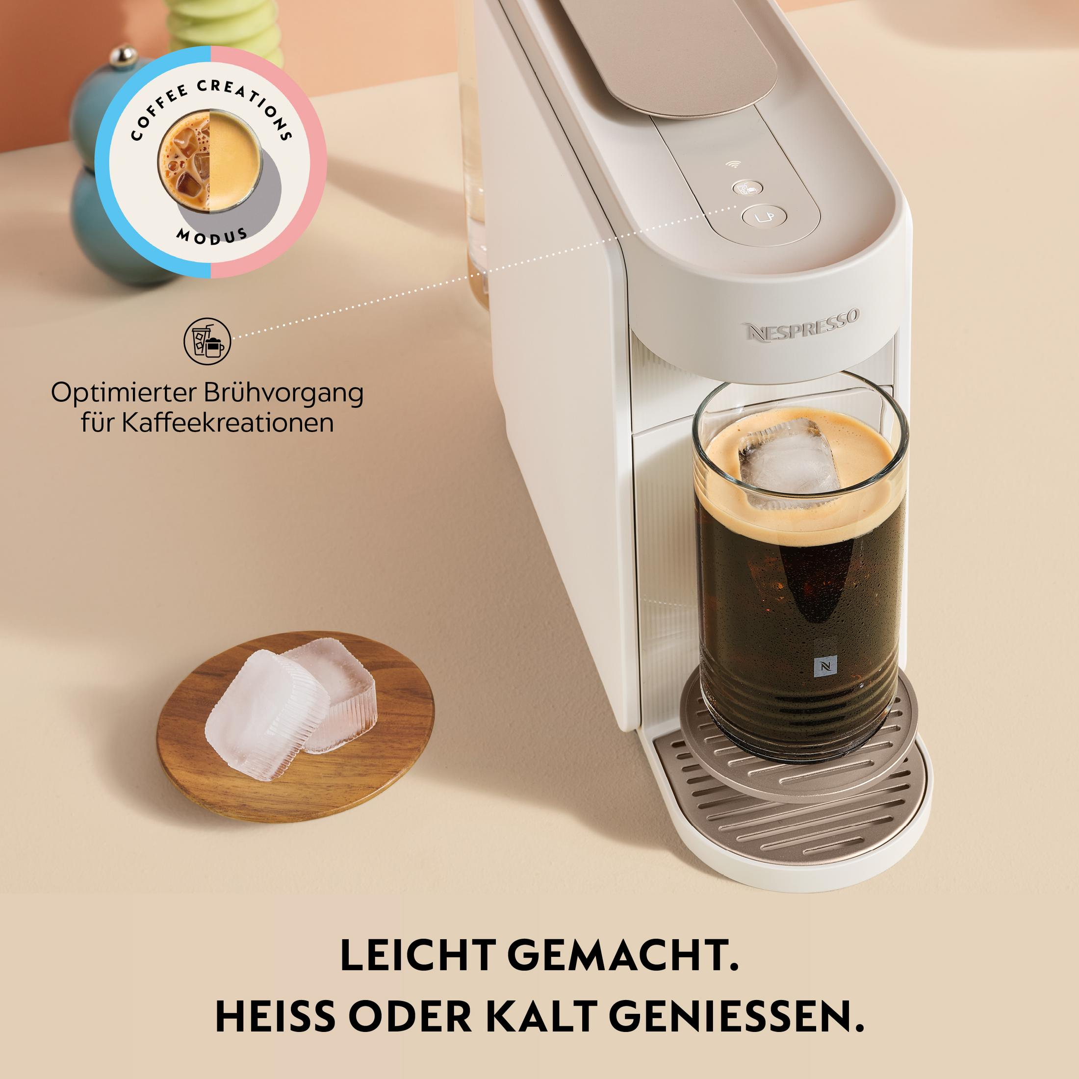 Eine weiße Nespresso-Maschine mit einem Glas Eiskaffee und Eiswürfeln auf einem Holzteller.