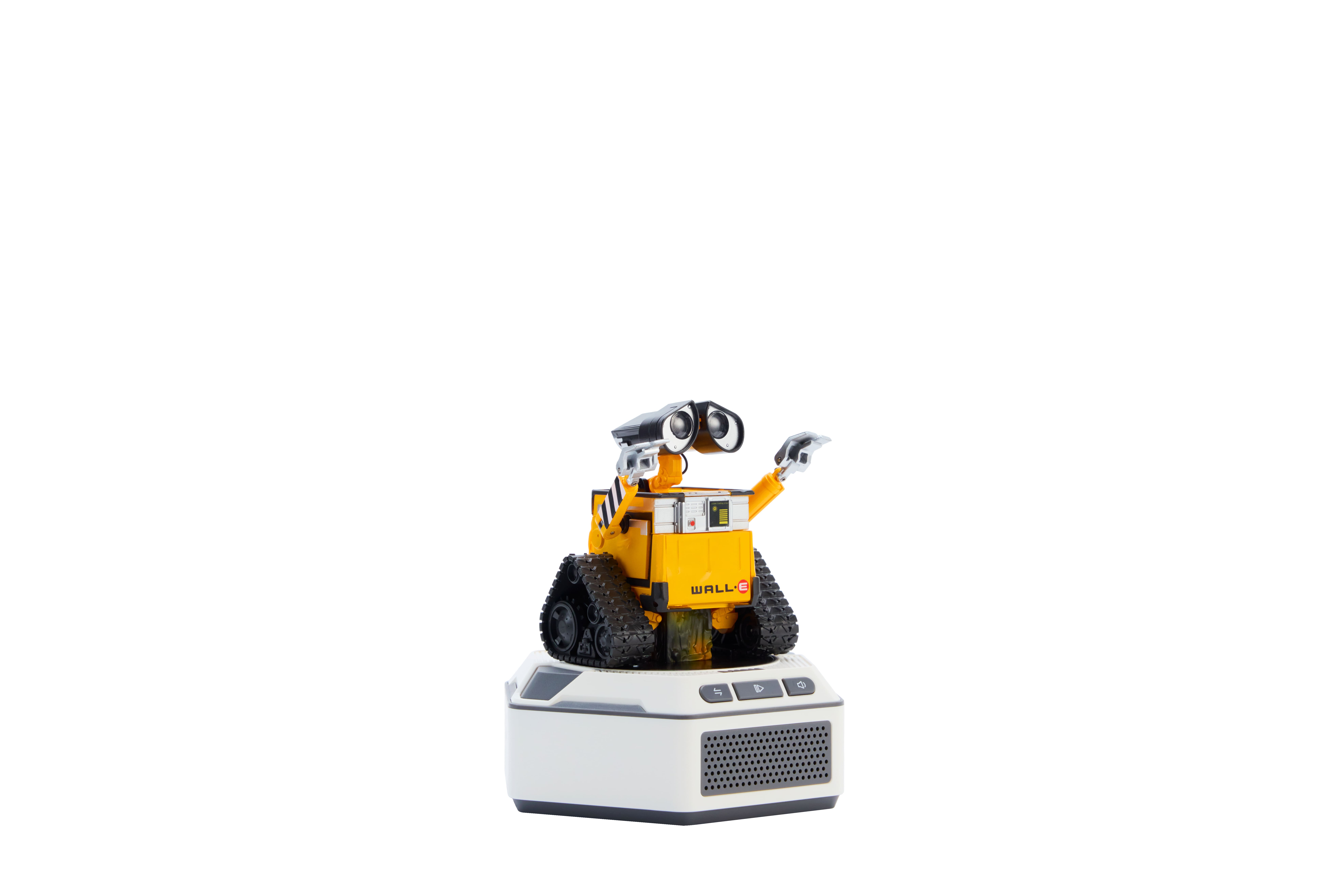 Una figura de robot amarilla con orugas se alza sobre una base blanca con altavoces.