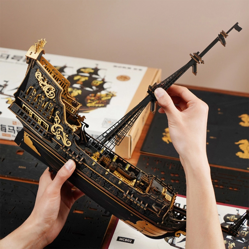 Une personne tient une maquette détaillée de bateau en bois noir et or.