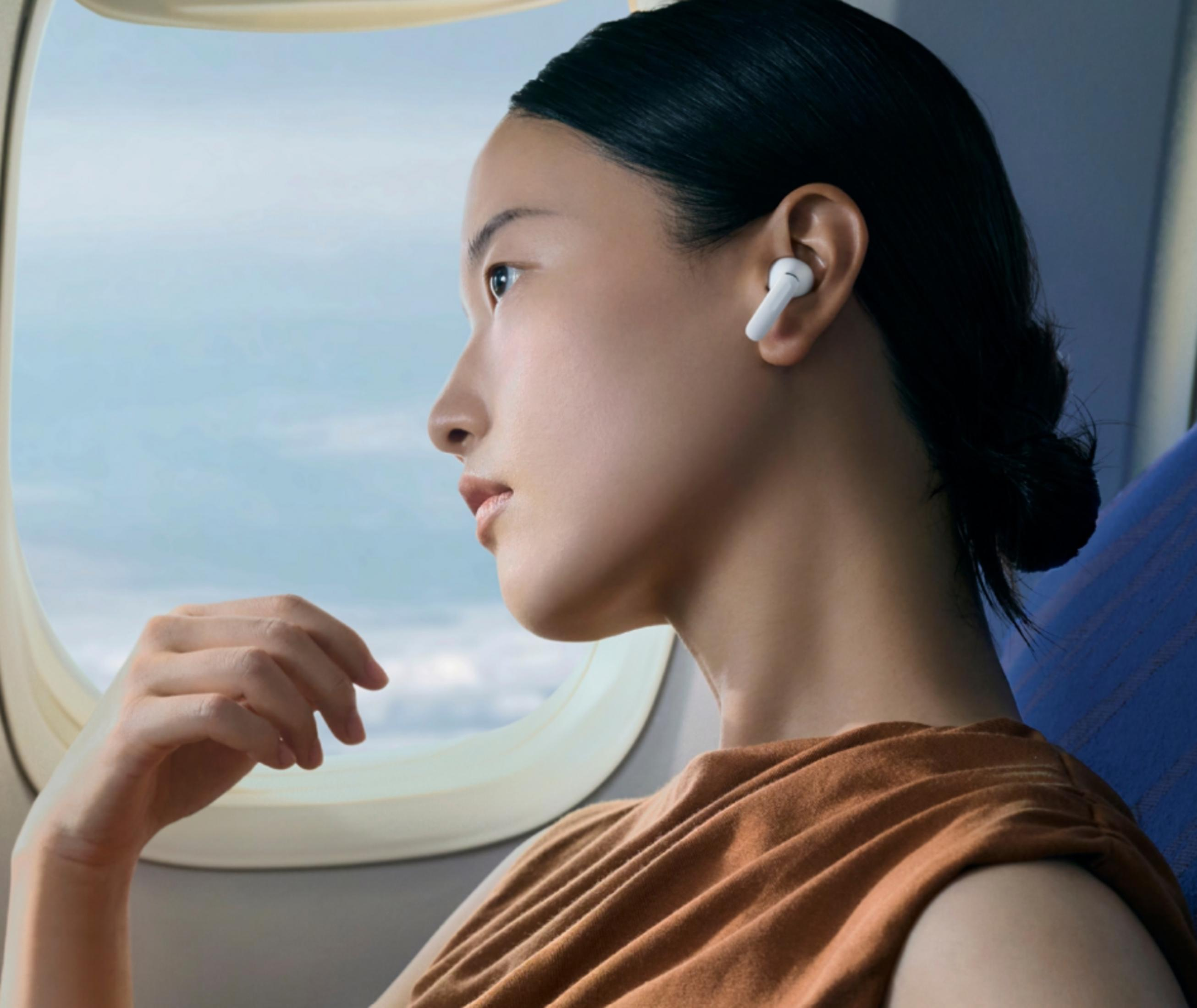 Donna con auricolari guarda fuori oblò aereo, indossa maglia marrone.