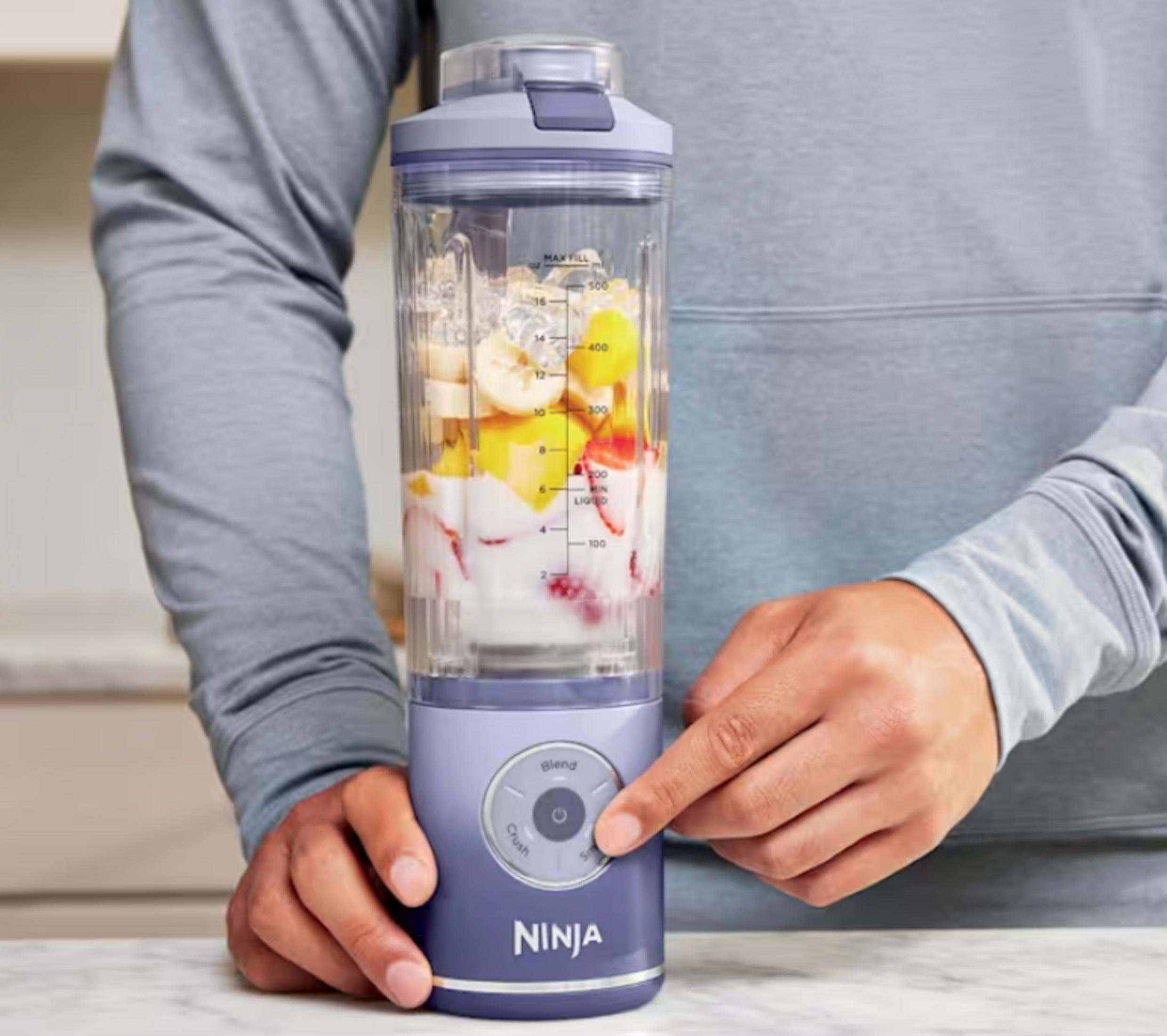 Un frullatore Ninja viola pieno di frutta e ghiaccio, pronto per frullare.