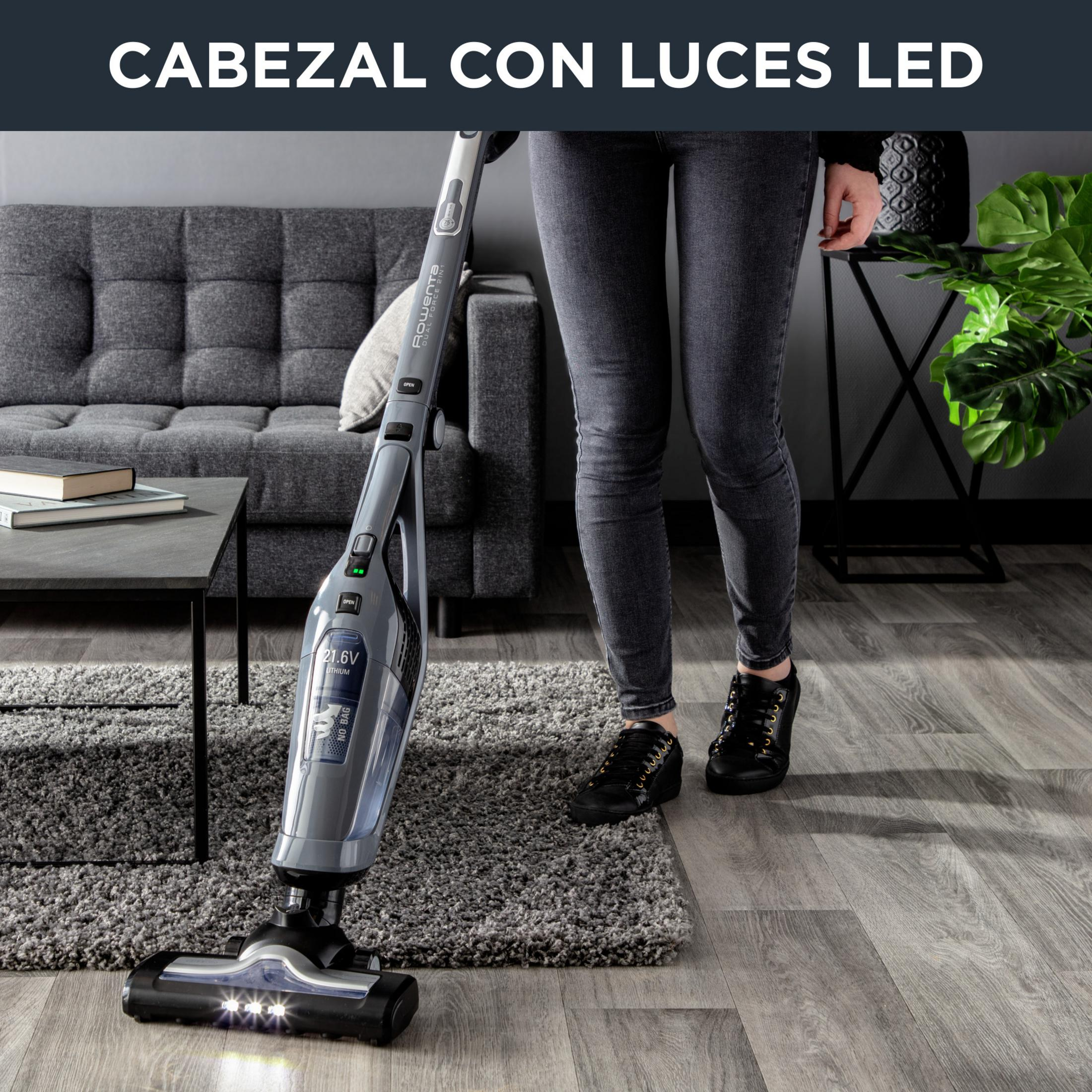 Una aspiradora inalámbrica gris con luces LED limpia una alfombra de sala.