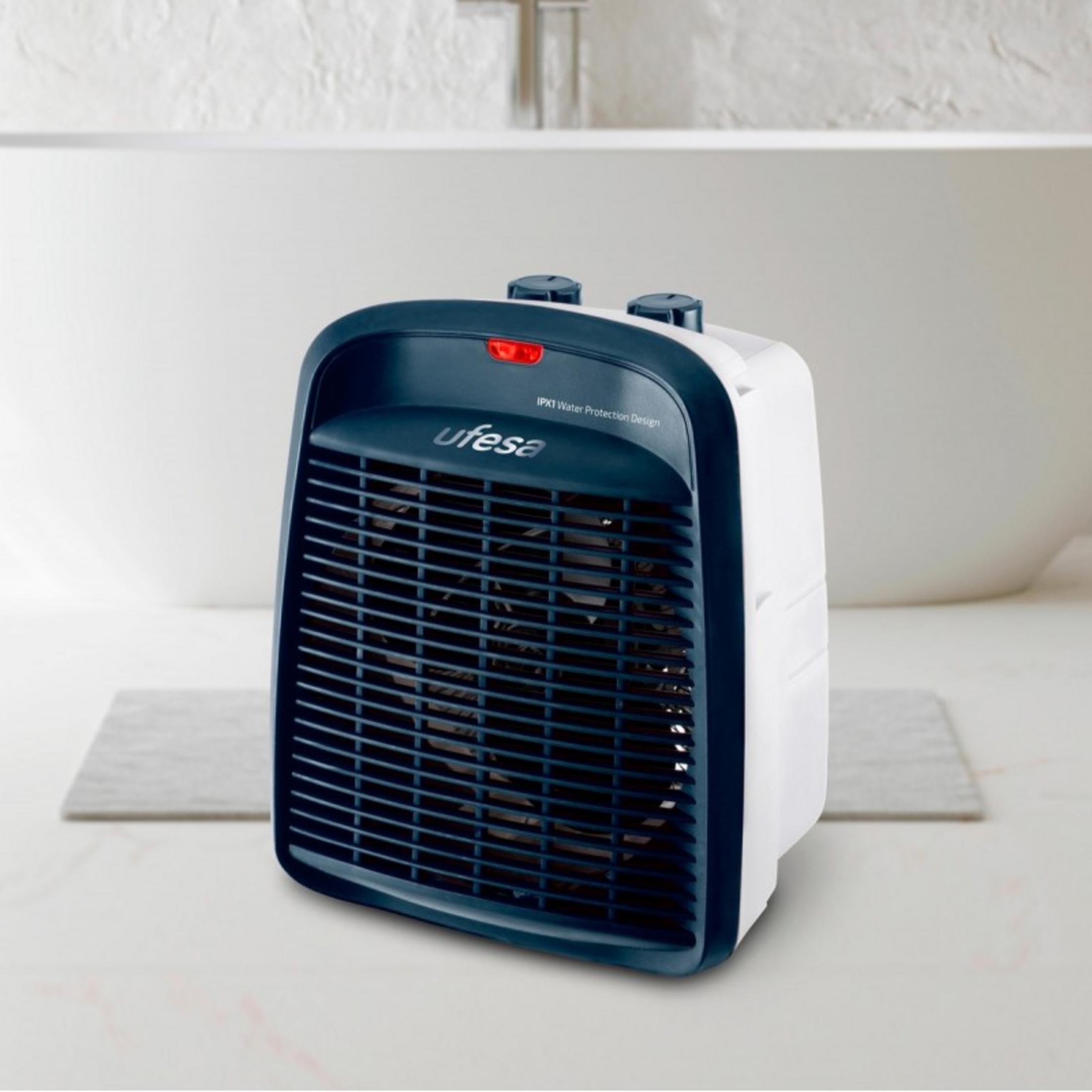 Un calefactor blanco y azul oscuro con rejilla y controles, colocado sobre una superficie.