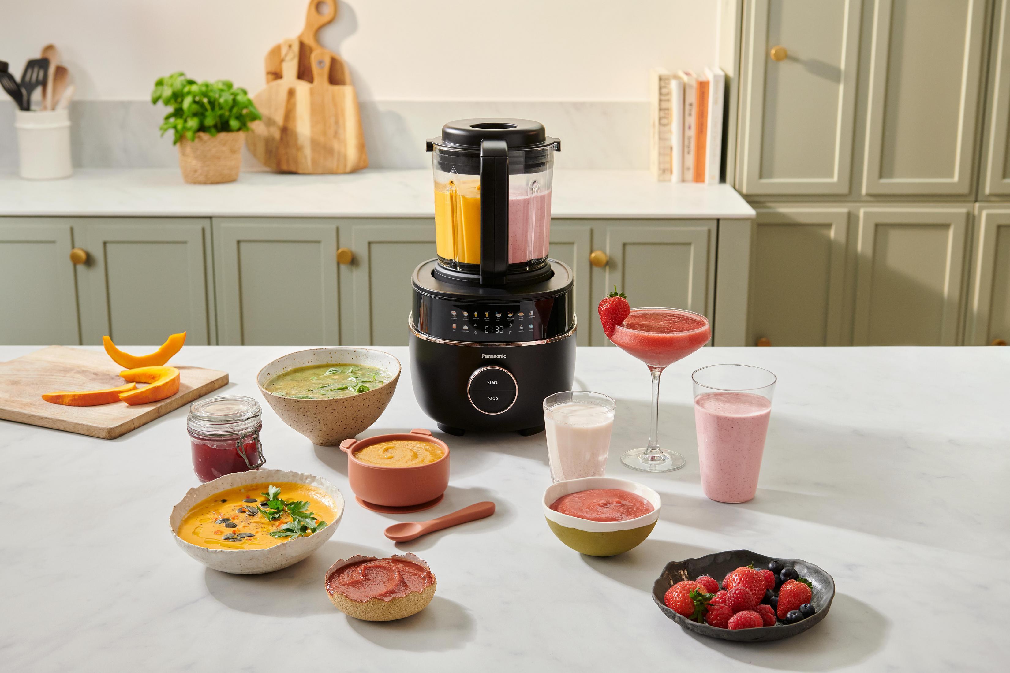Ein Mixer mit gefüllt Behältern, daneben Schüsseln mit Suppe und Beeren.