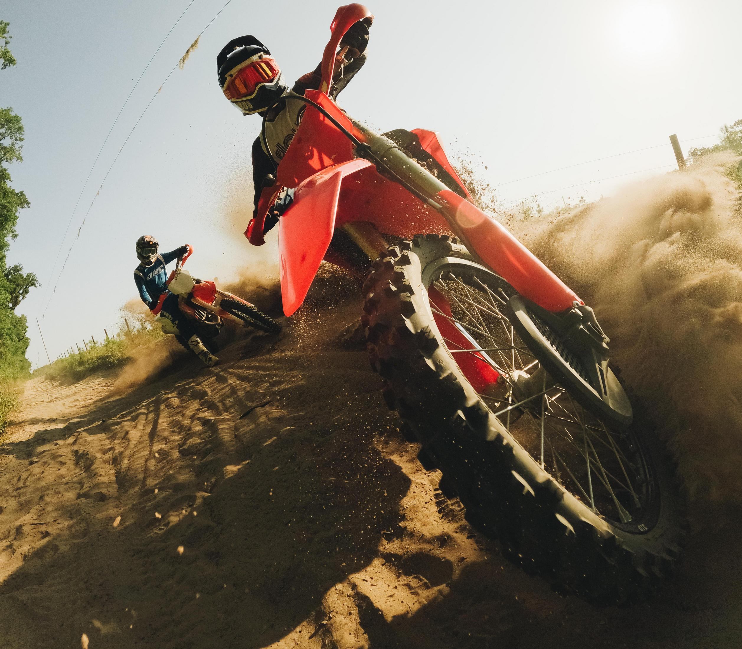 Dos pilotos de motocross corren en una pista polvorienta, uno delante, el otro detrás.