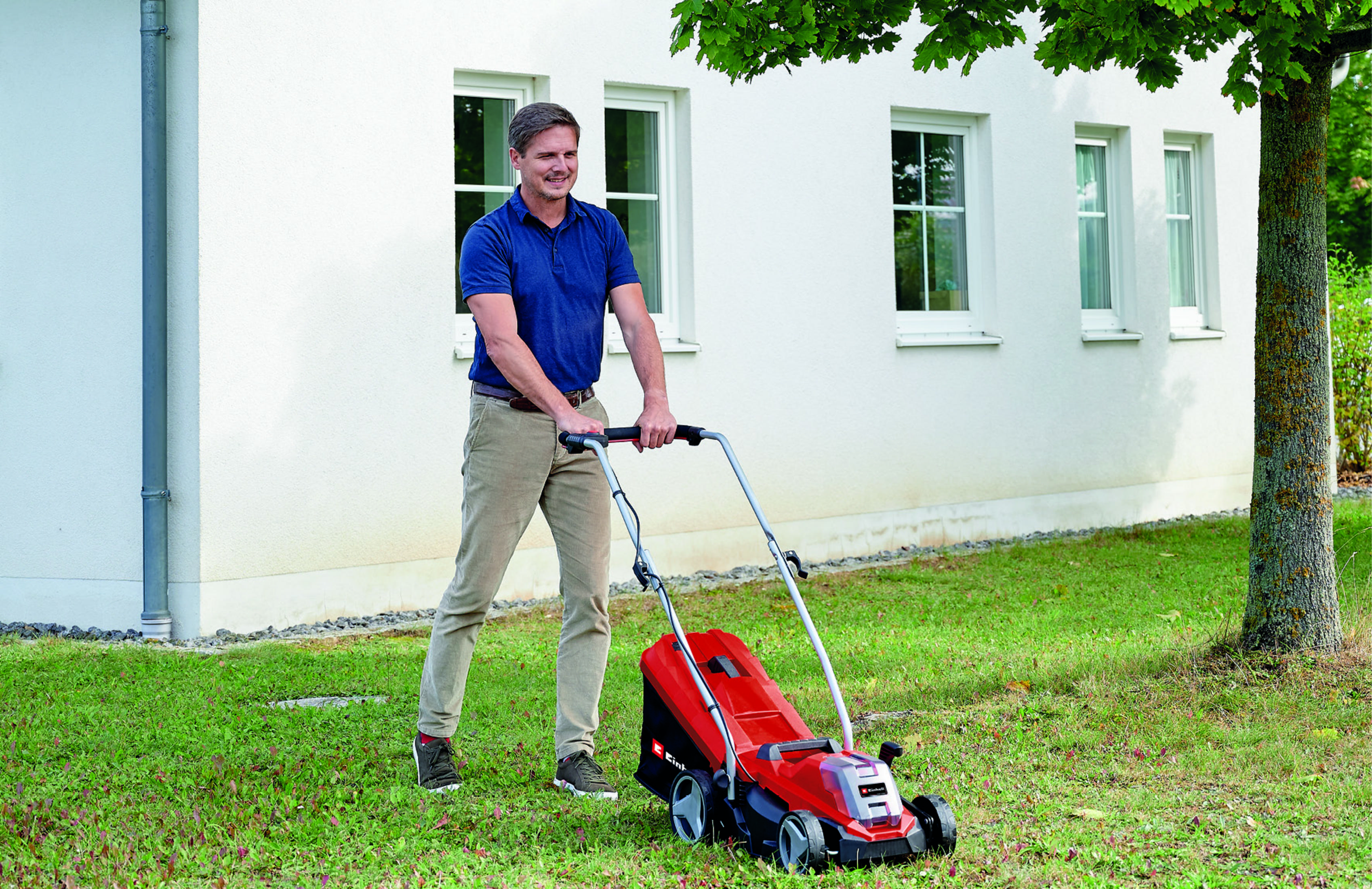 Ein Mann mäht den Rasen mit einem roten Elektrorasenmäher vor einem weißen Haus.