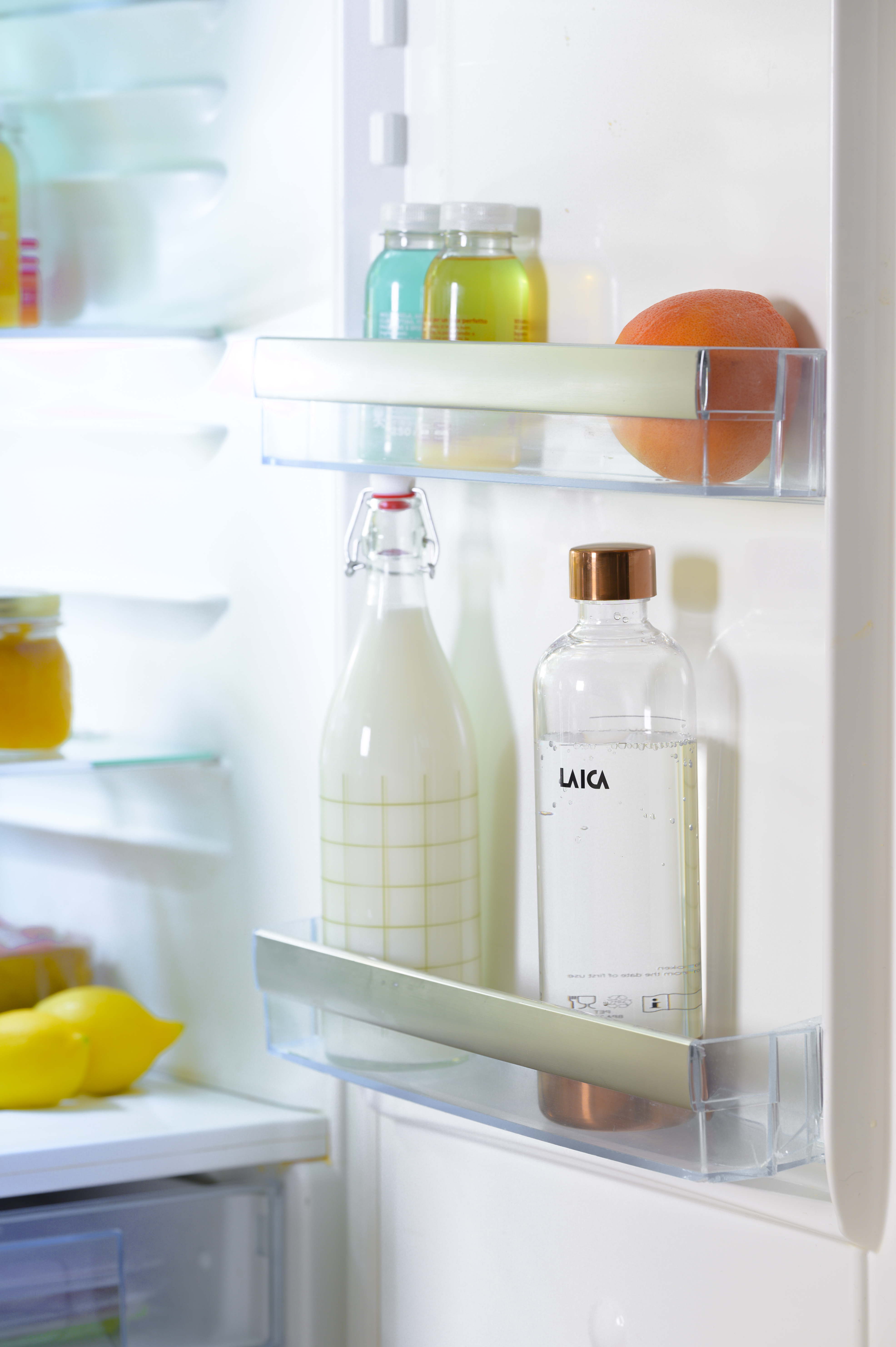 Interior de un refrigerador con estantes que sostienen botellas de leche, agua, jugo y una naranja.
