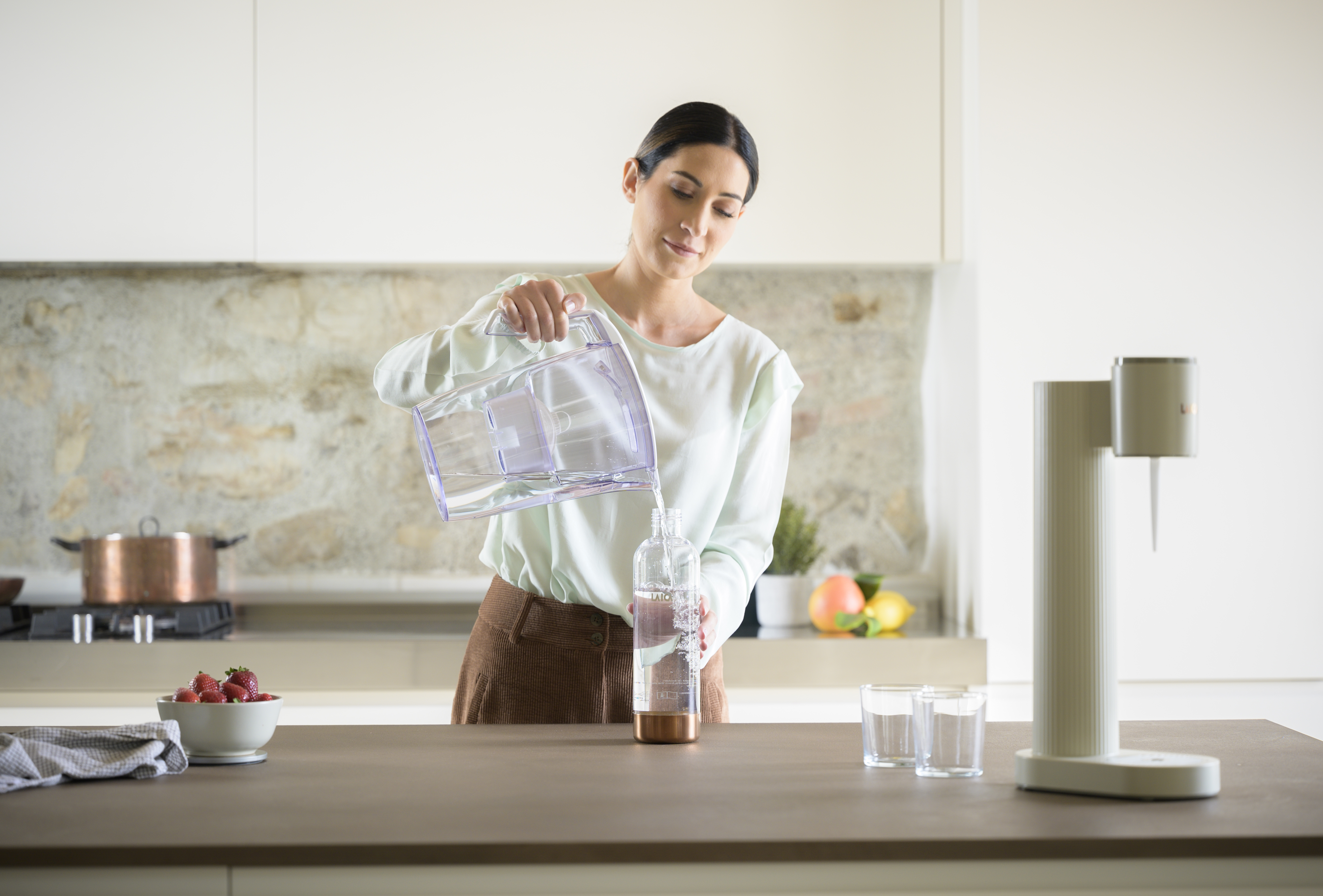 Una mujer vierte agua de una jarra a una botella en una cocina moderna.