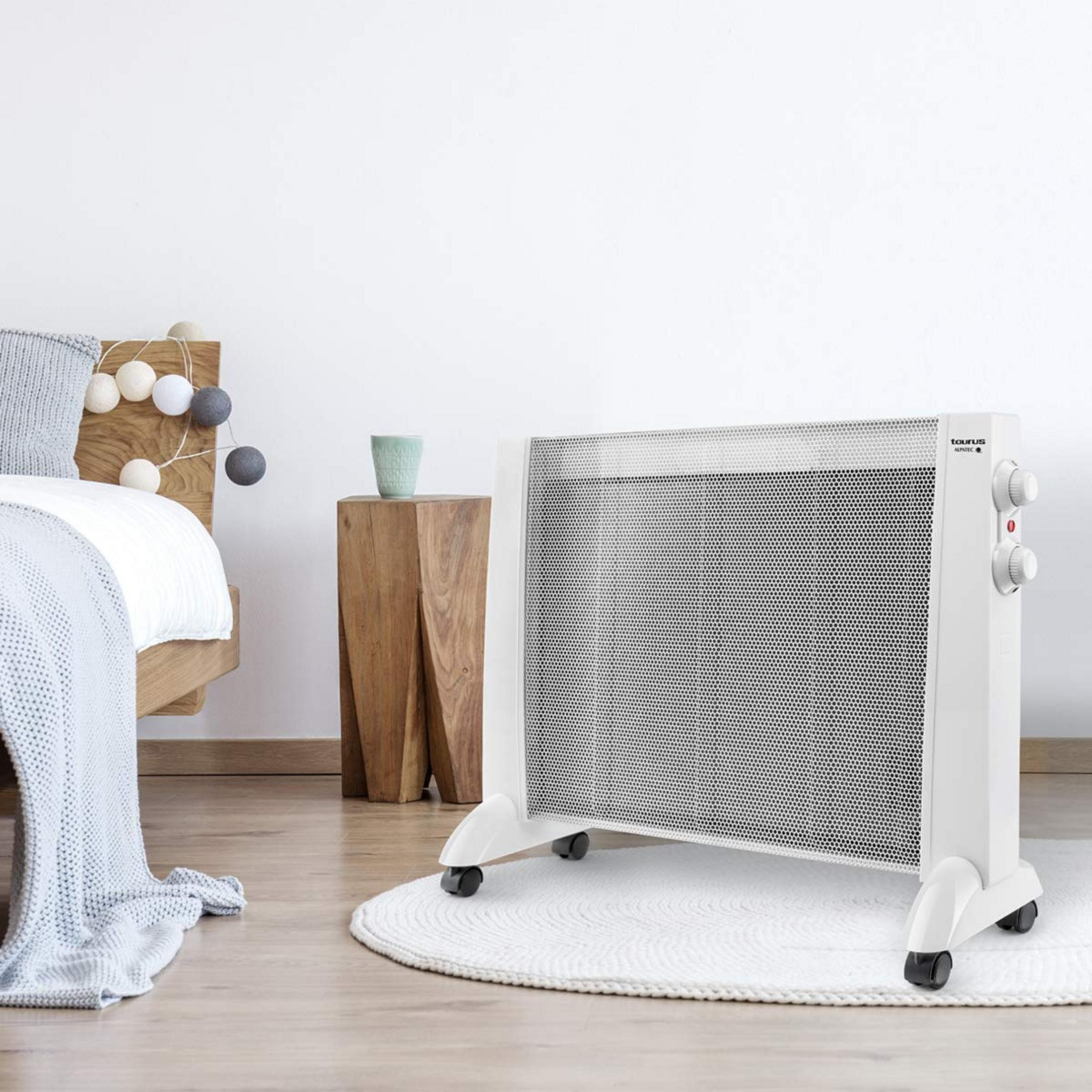 Una stufa elettrica bianca si trova su un tappeto rotondo accanto a un letto.