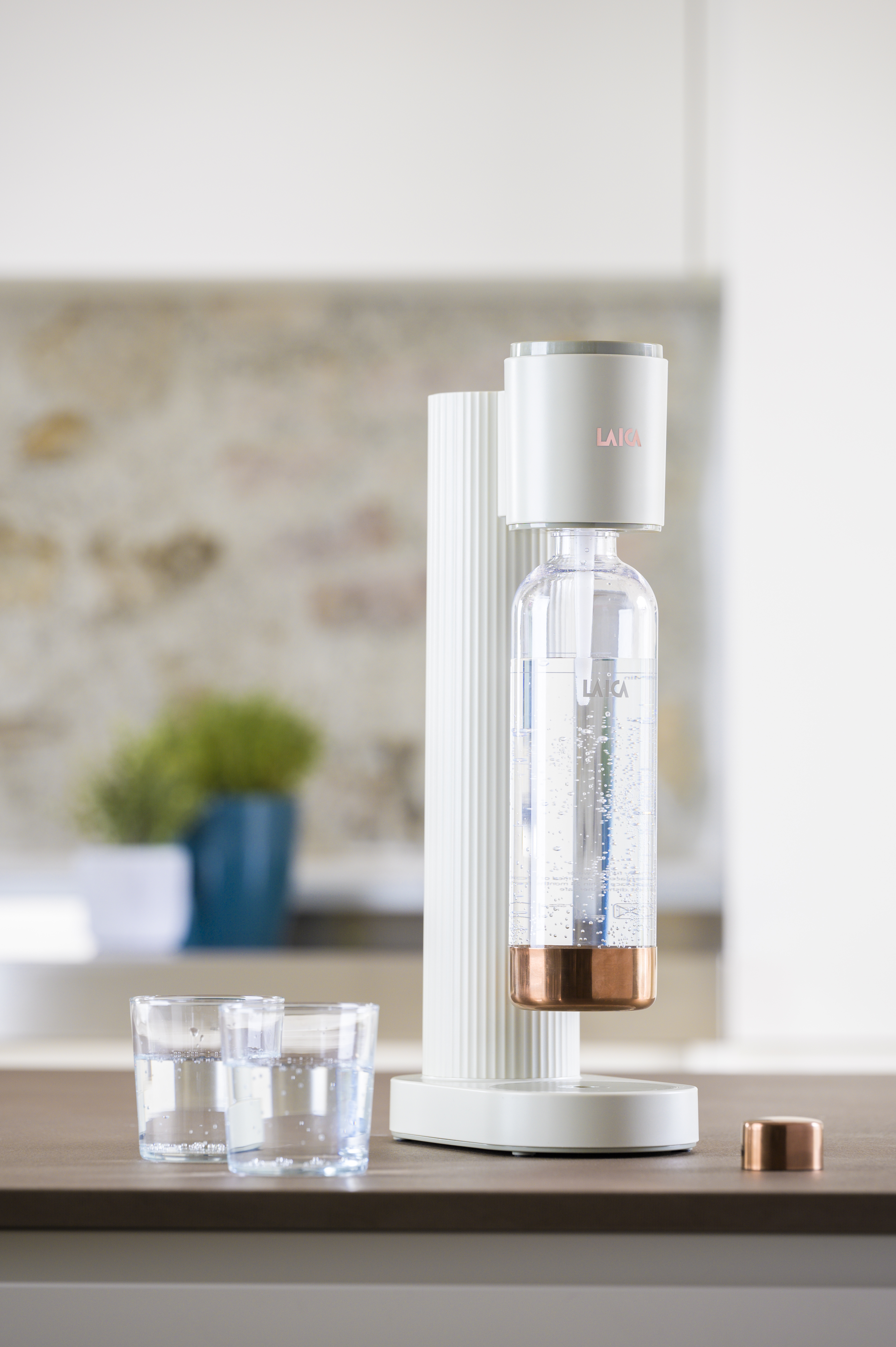 Un carbonatador de agua blanco con botella, dos vasos y una tapa de cobre.