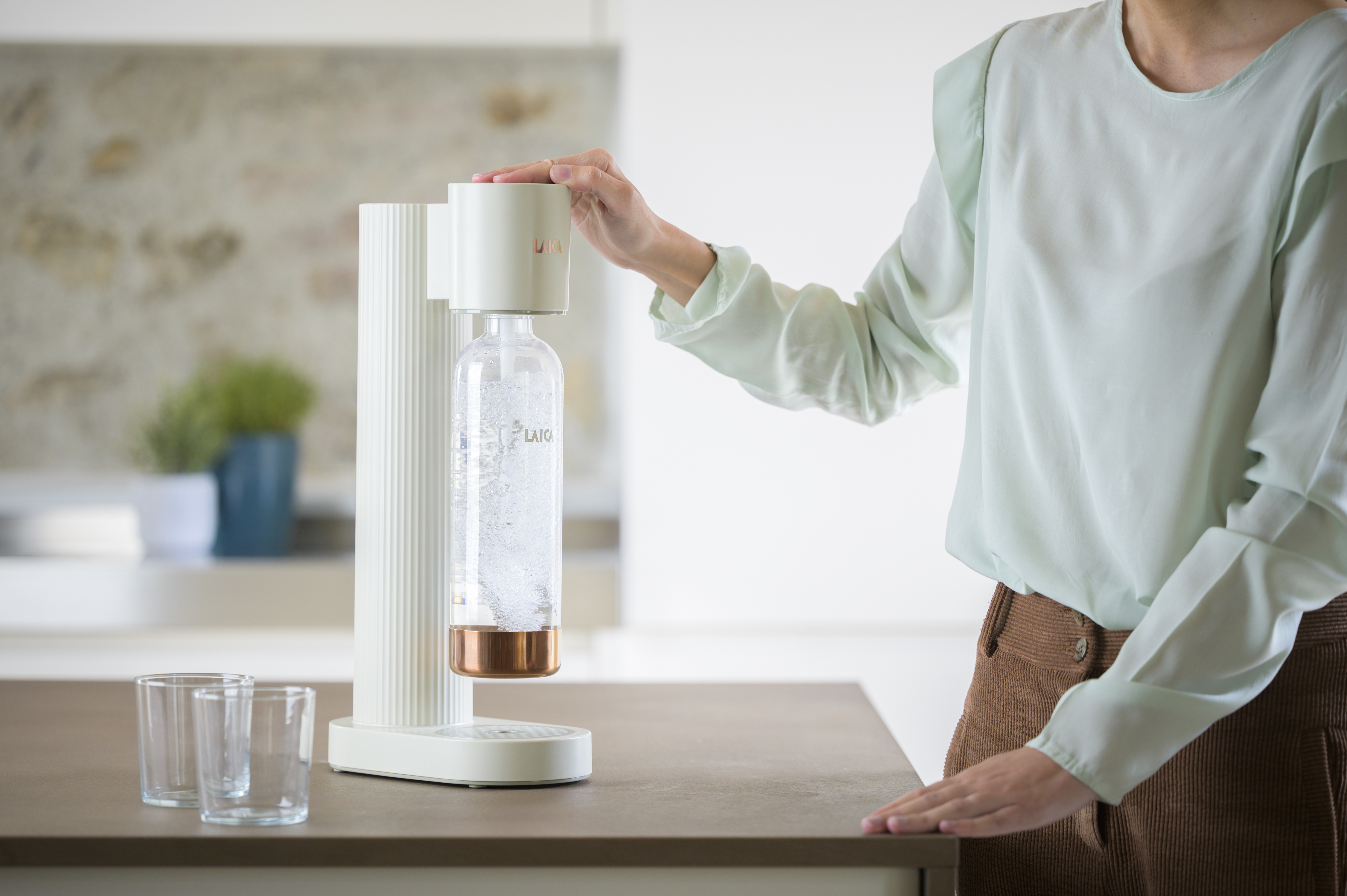 Una persona opera una máquina de soda con una botella y vasos sobre la mesa.