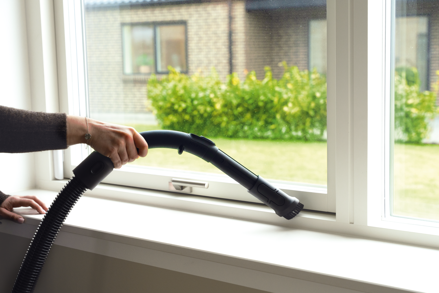 Eine Hand benutzt einen Staubsauger, um eine Fensterbank zu reinigen.